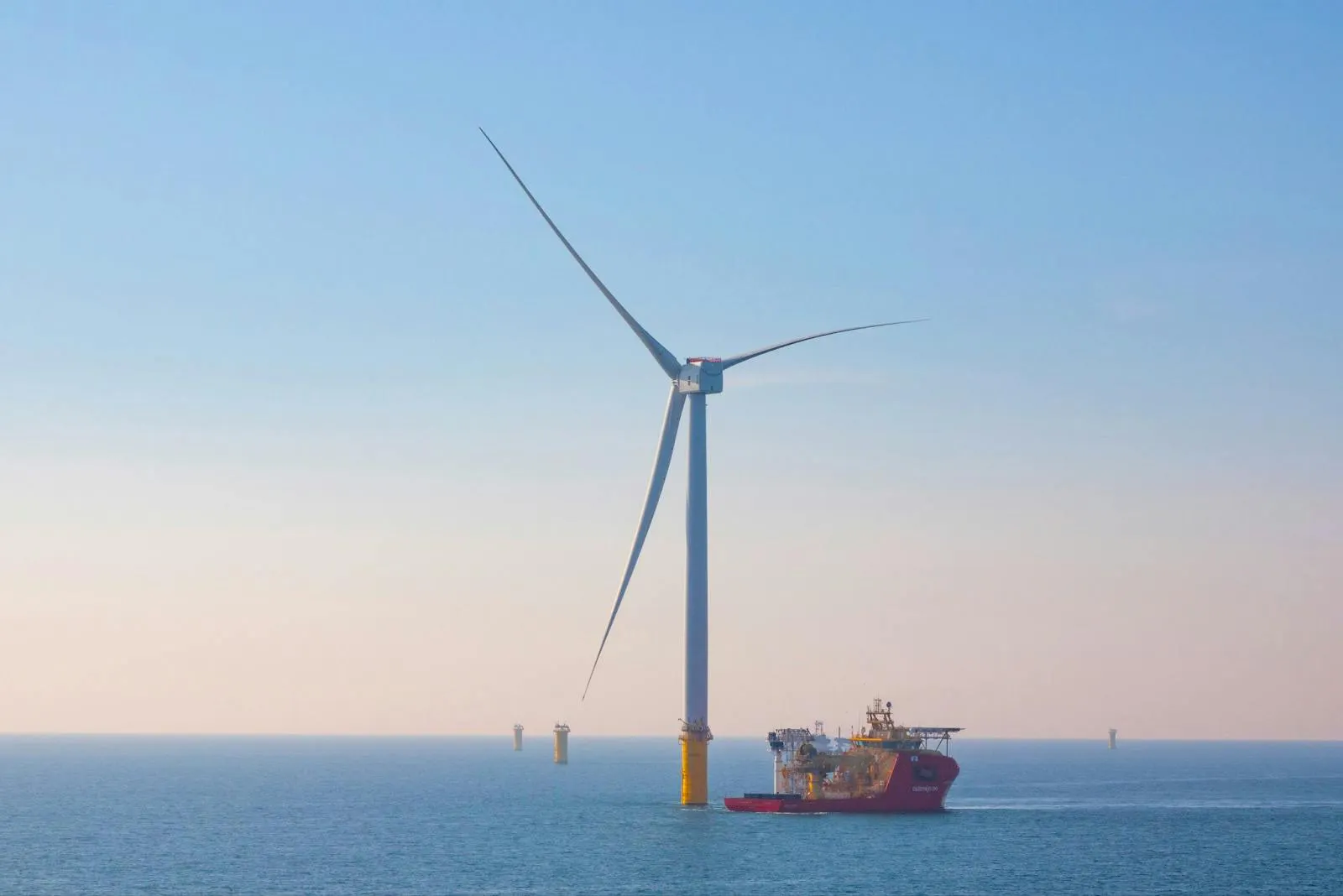 A single large offshore turbine on a yellow monopile at sea with a service vessel alongside