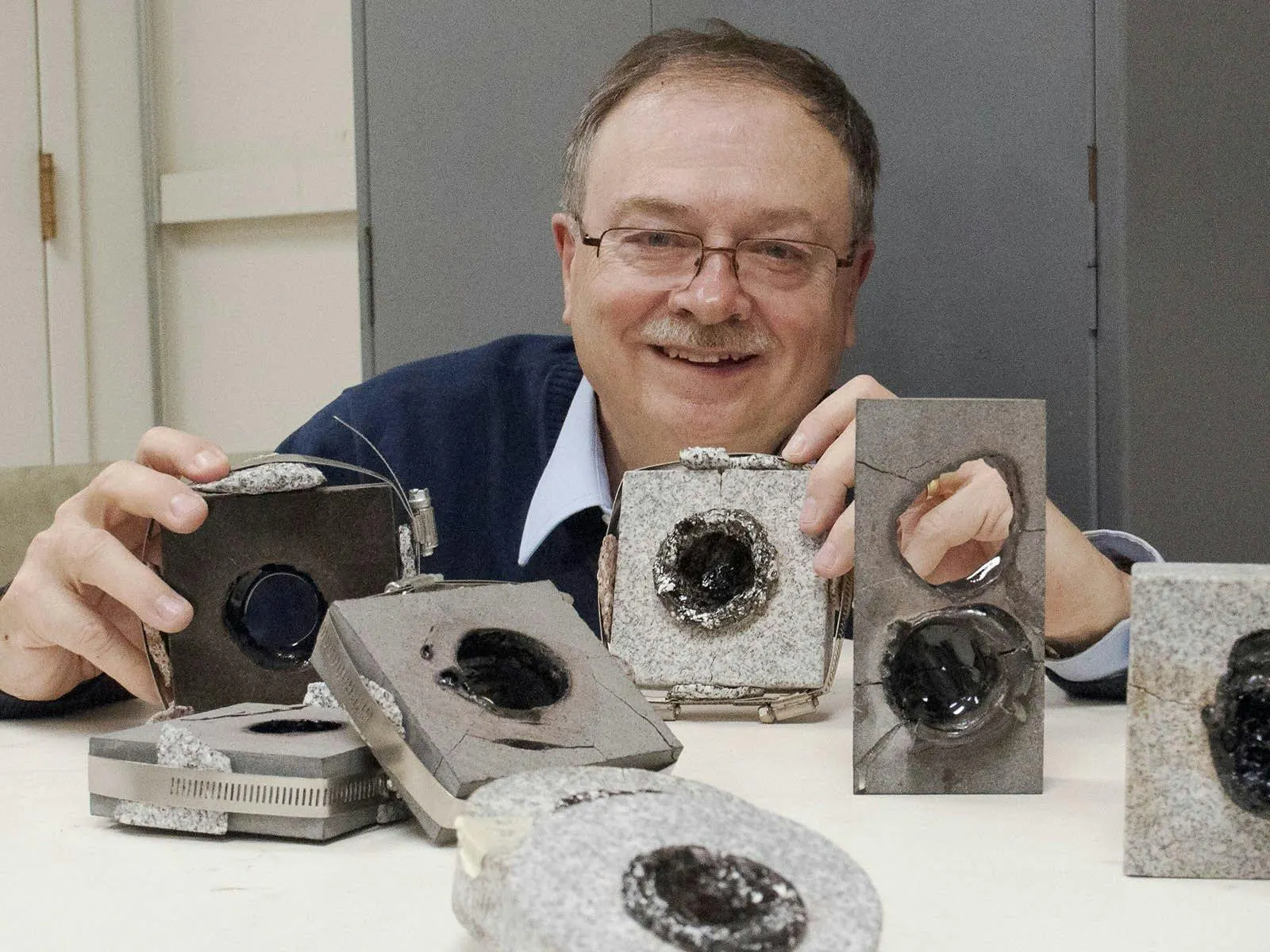 Researcher holding granite blocks bored through by millimetre-wave beams, more drilled samples on the table