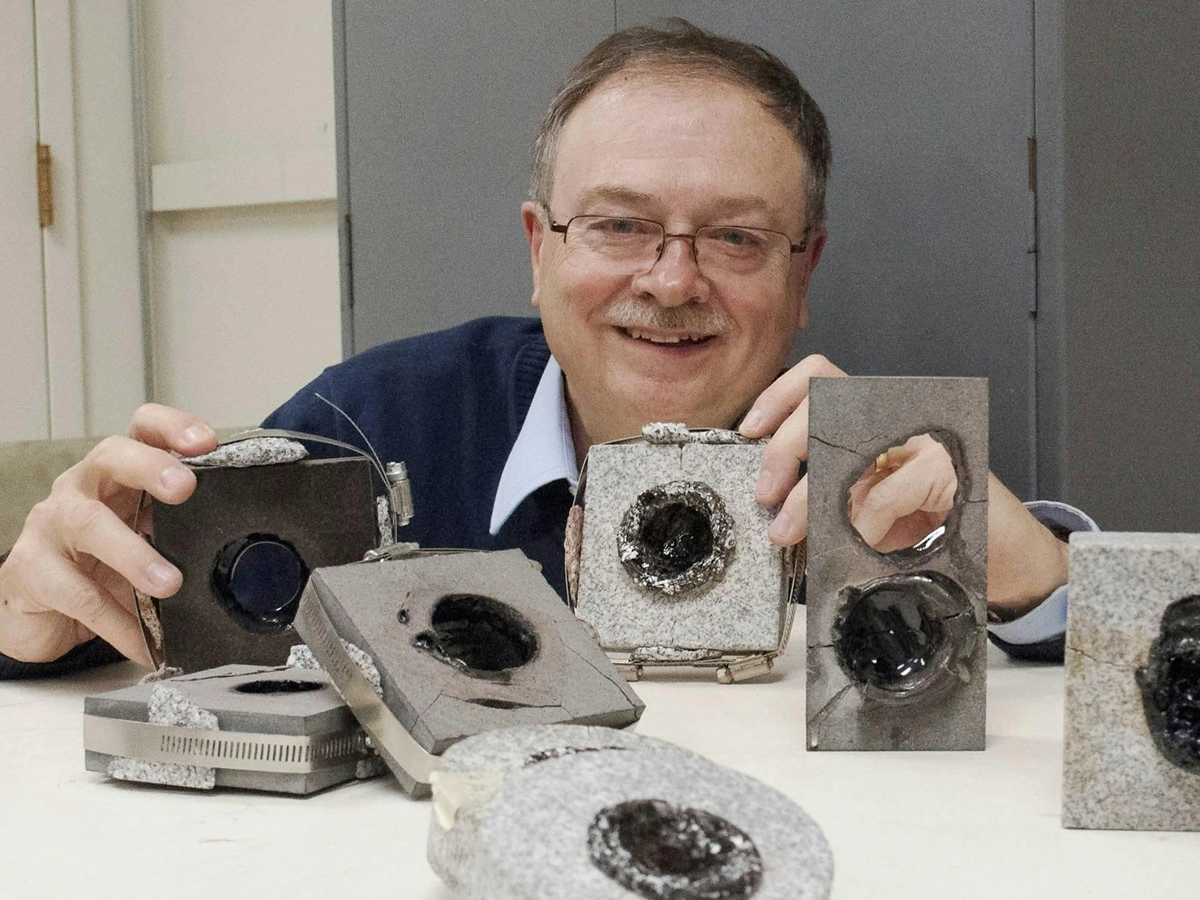 Researcher holding granite blocks bored through by millimetre-wave beams, more drilled samples on the table