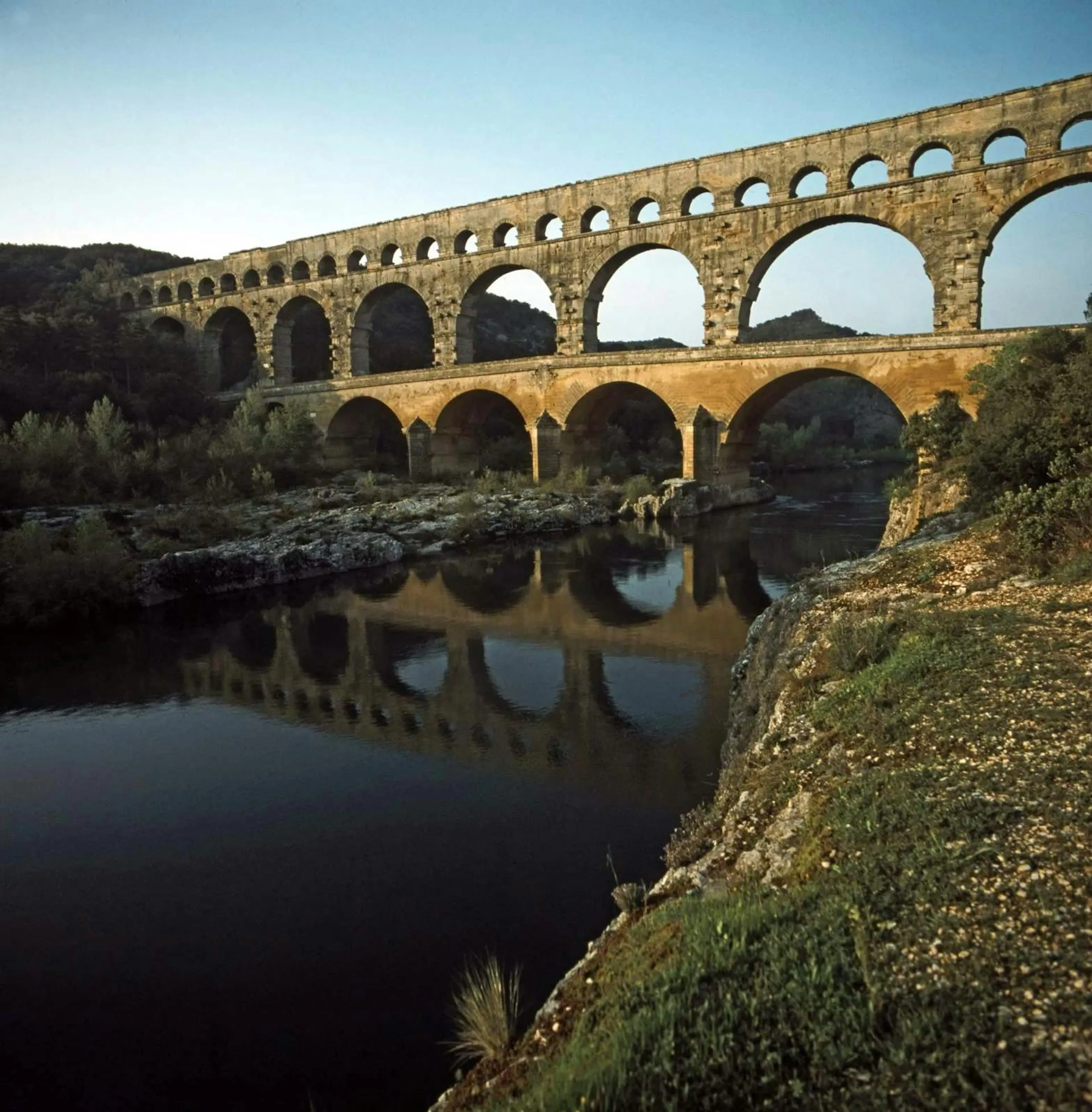 Photograph of the Pont du Gard Roman aqueduct, tiers of stone arches reflected in the river below