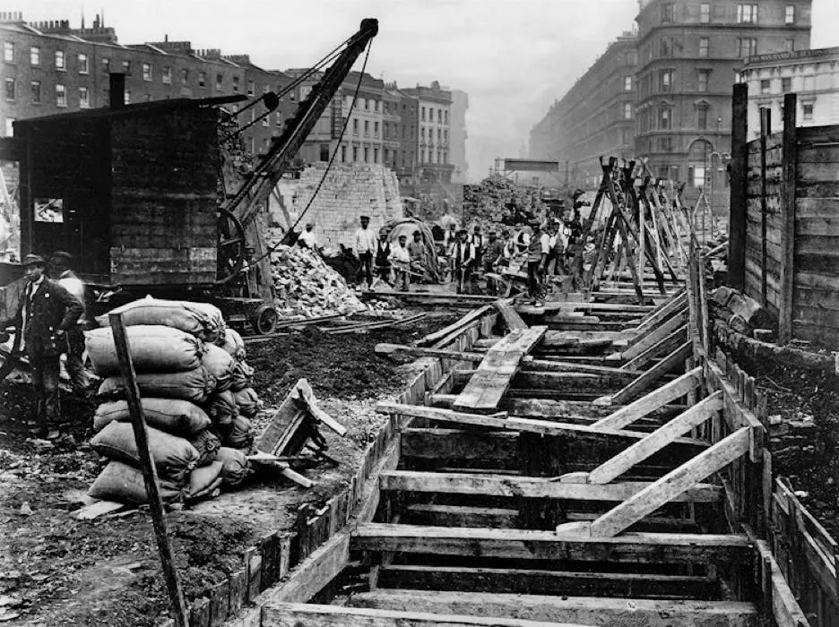 Black-and-white photograph of cut-and-cover subway construction, timber shoring in an open trench along a city street
