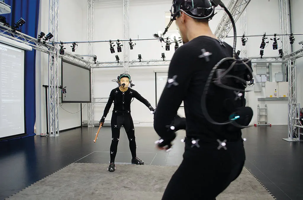 Photograph of a motion capture stage, performers in marker suits and head-mounted cameras surrounded by tracking rigs