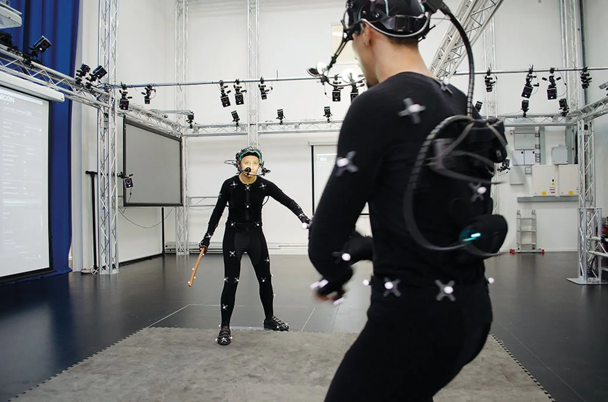 Photograph of a motion capture stage, performers in marker suits and head-mounted cameras surrounded by tracking rigs