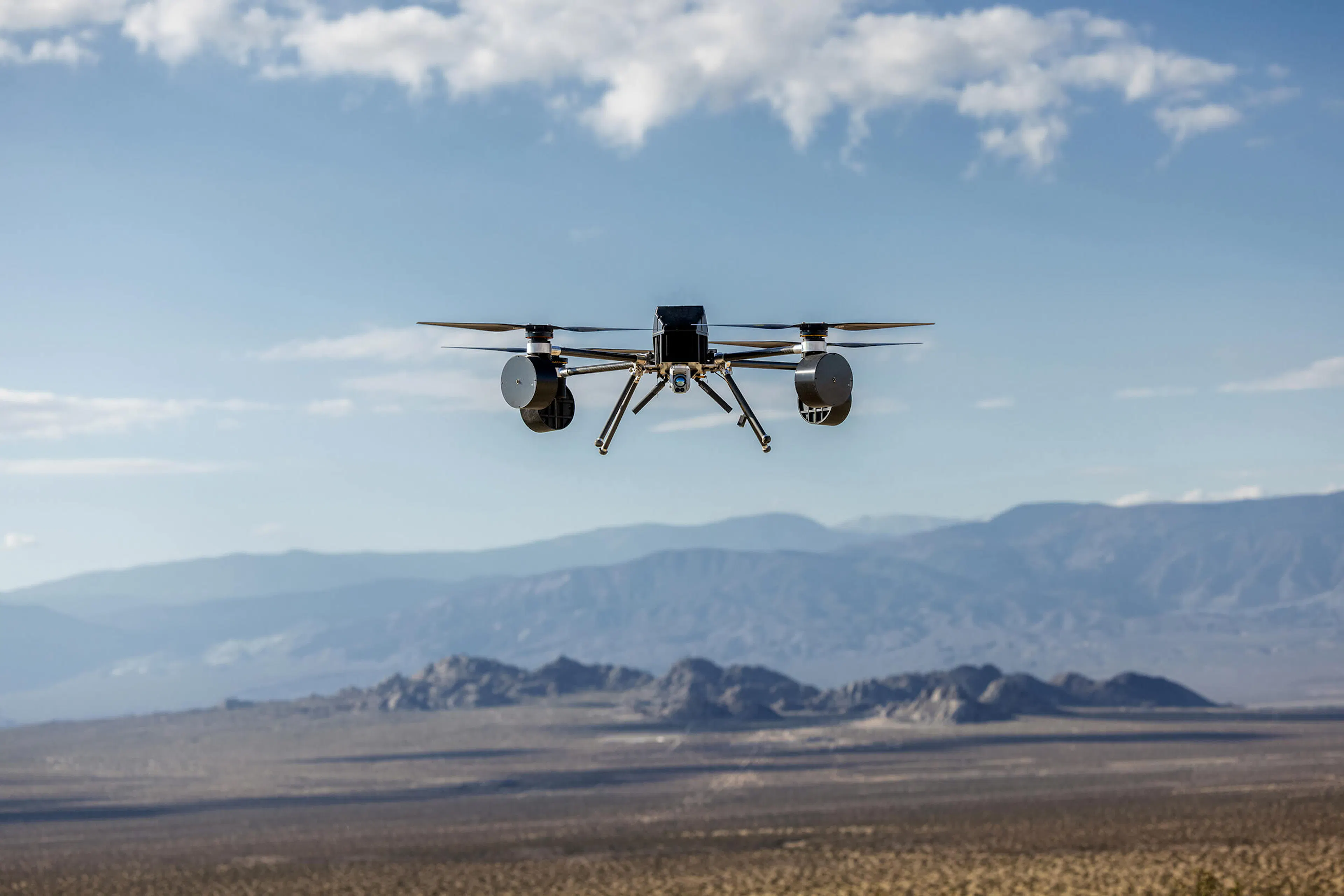 CX2's Wraith drone in flight over a desert valley, a black quadcopter with a cylindrical RF sensor pod on each side and a gimbaled camera beneath the body.