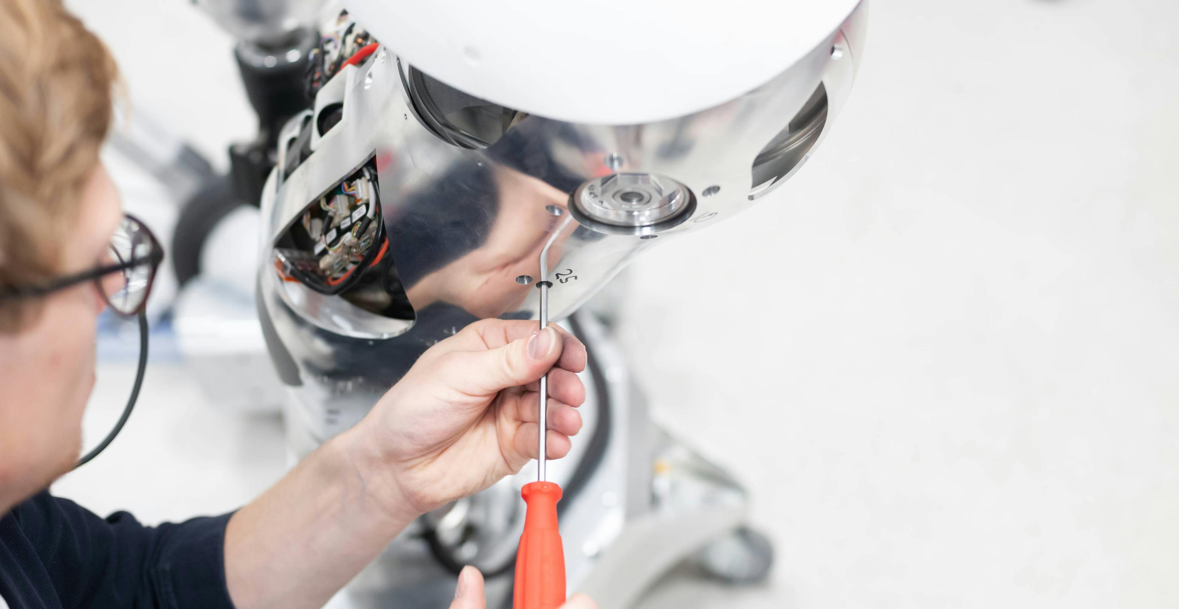 1X engineer working on a robot in a manufacturing facility