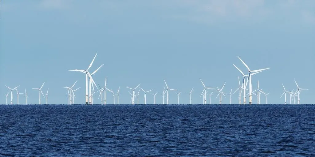 A row of offshore wind turbines on the horizon above dark open water