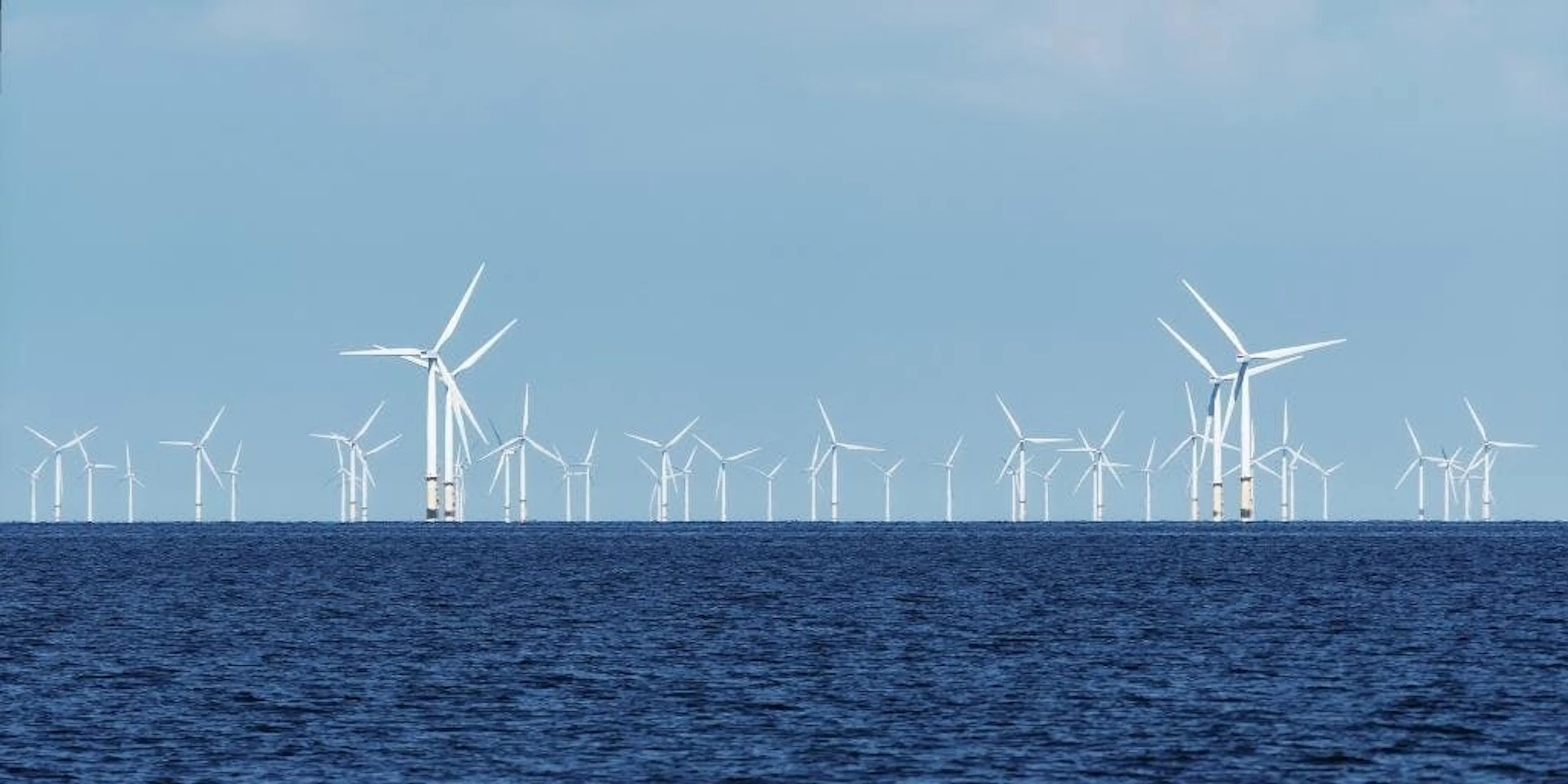 A row of offshore wind turbines on the horizon above dark open water
