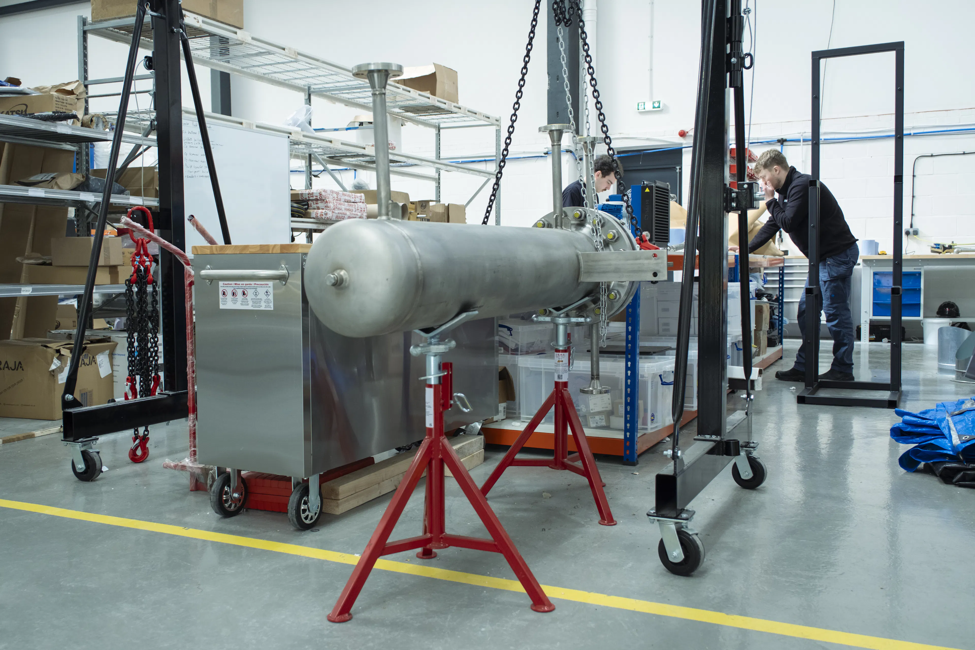 Two Rivan engineers assembling a large stainless-steel pressure vessel on stands in the company's London workshop