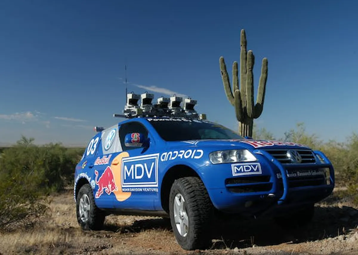 Photograph of Stanford's blue DARPA Grand Challenge vehicle, roof-mounted lidar units above desert scrub
