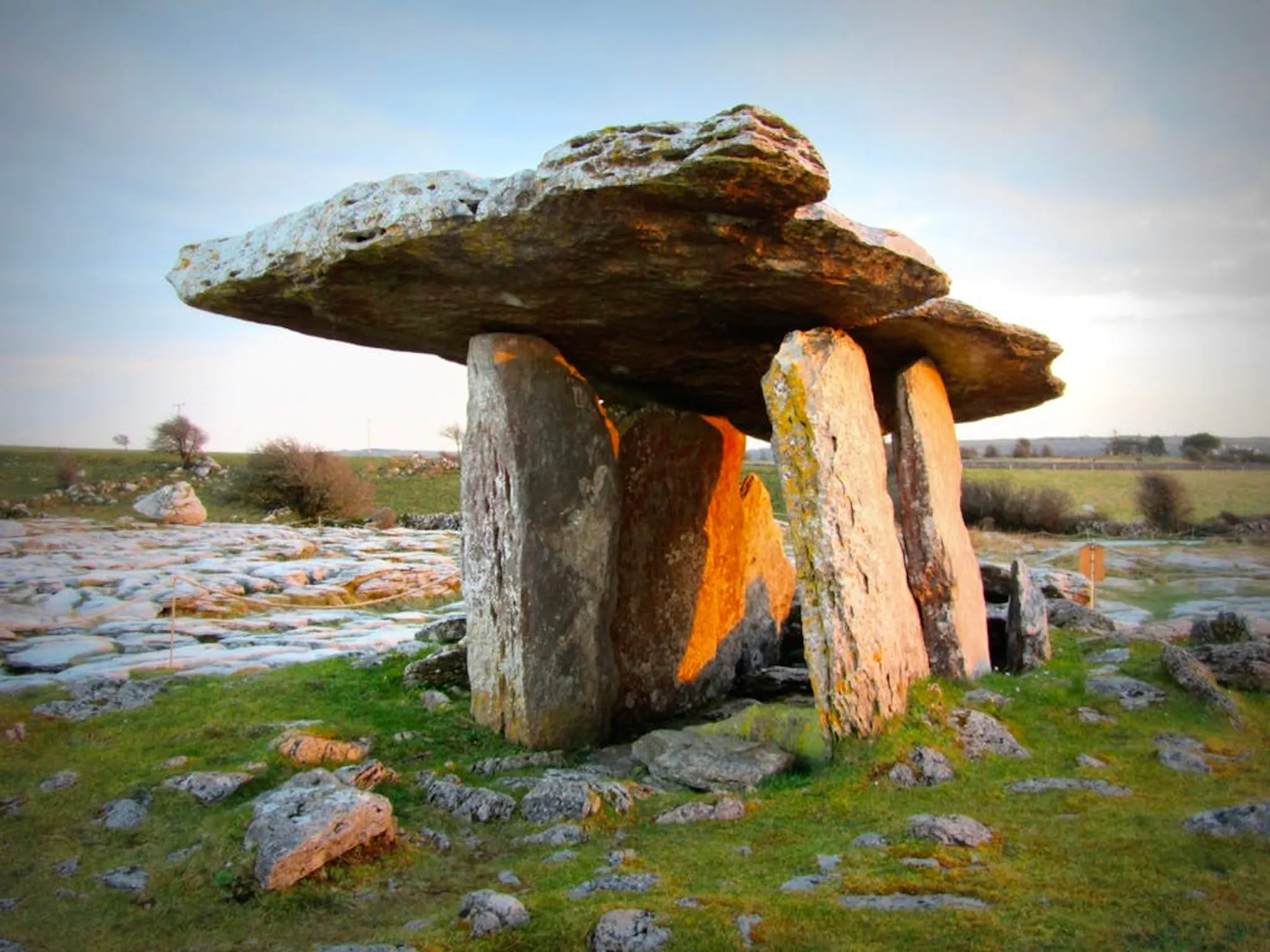 Photograph of a prehistoric dolmen, a broad capstone resting on upright stones in a rocky green field