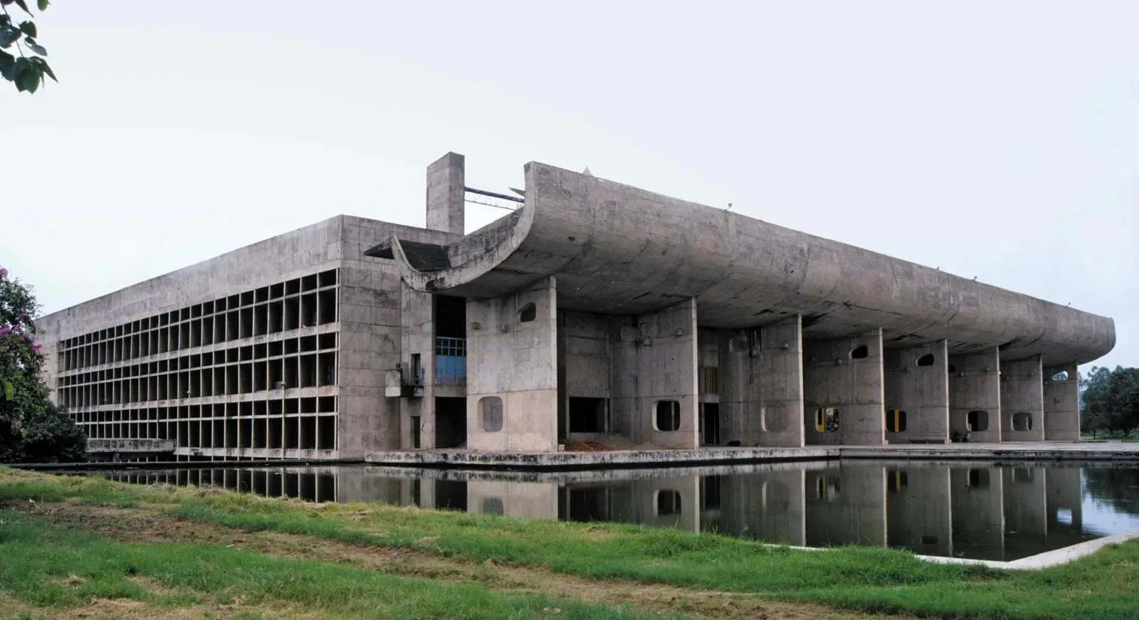 Photograph of Le Corbusier's Palace of Assembly at Chandigarh, its raw concrete portico reflected in a pool