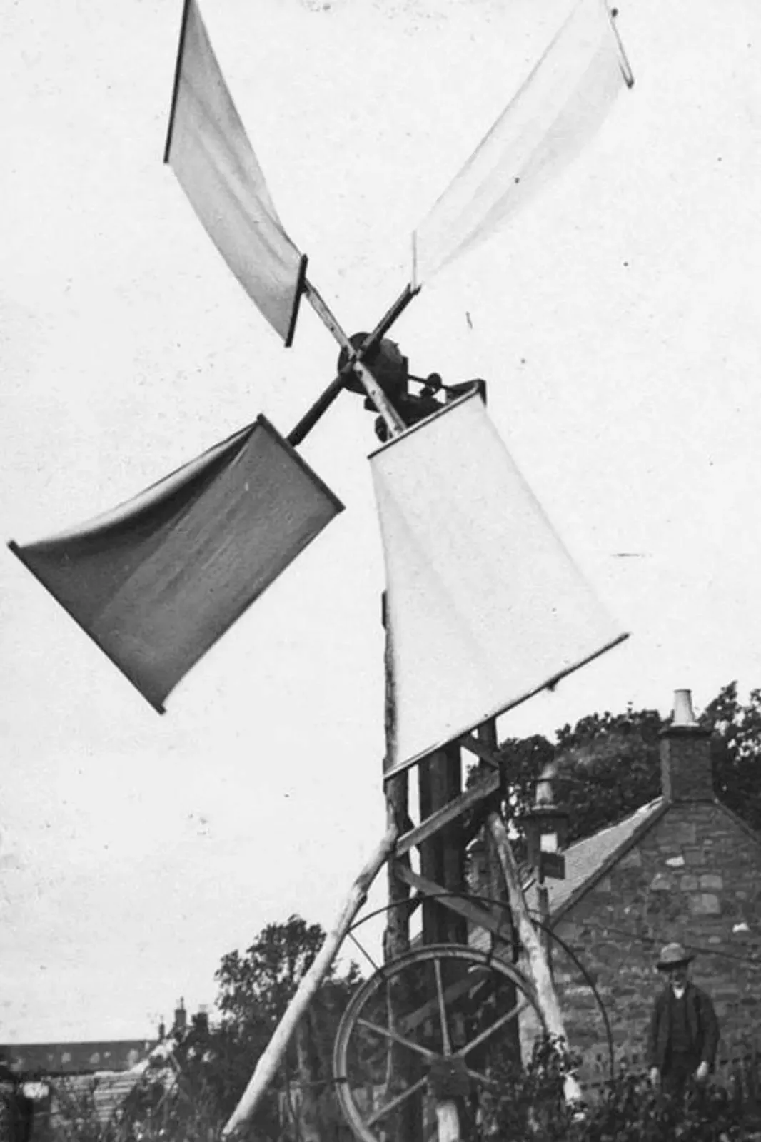 Black-and-white photograph of James Blyth's 1887 cloth-sailed windmill beside a stone cottage, a man standing at its base