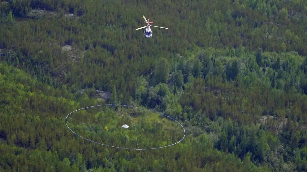 Helicopter towing a large circular transmitter loop over forest during an airborne geophysical survey