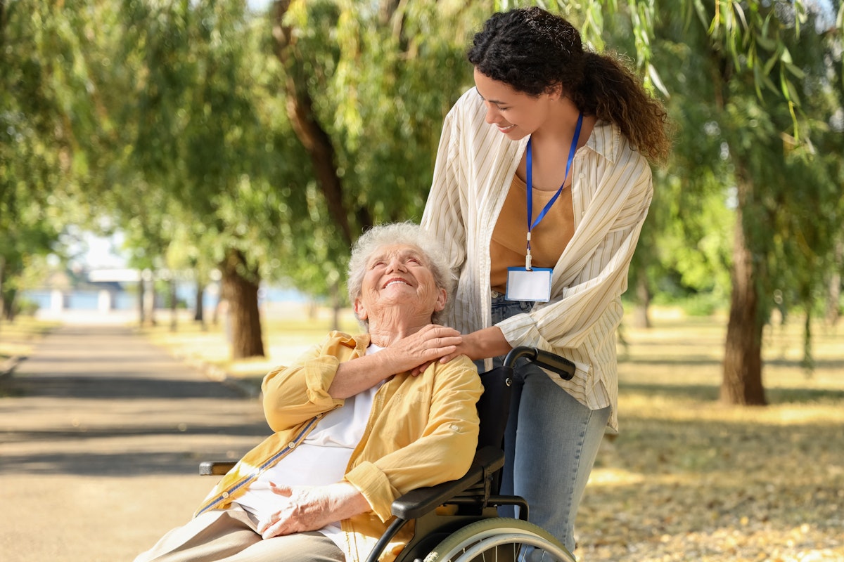 Care worker taking elderly woman for a walk outside in a park