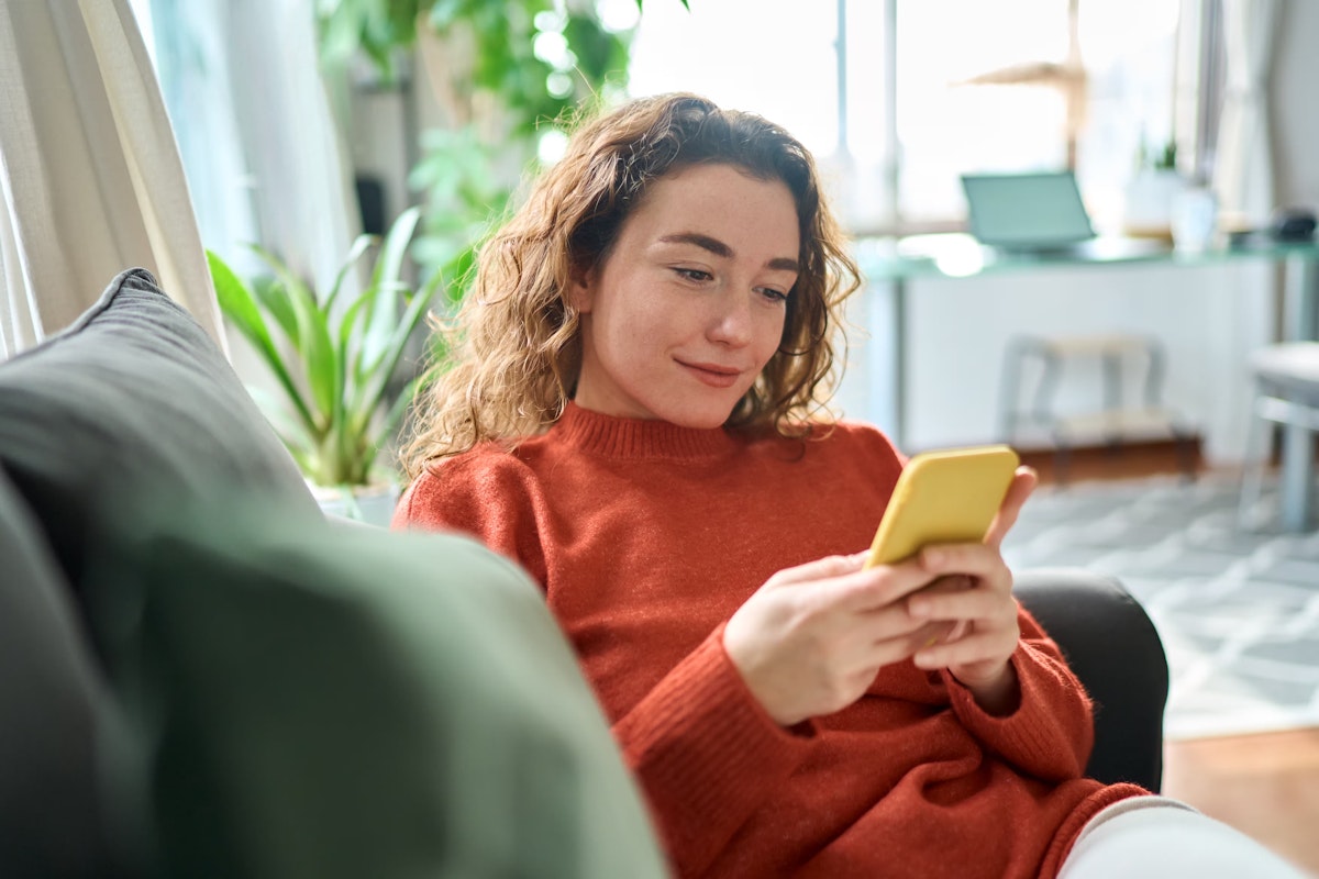 young woman sitting on couch looking at her smartphone