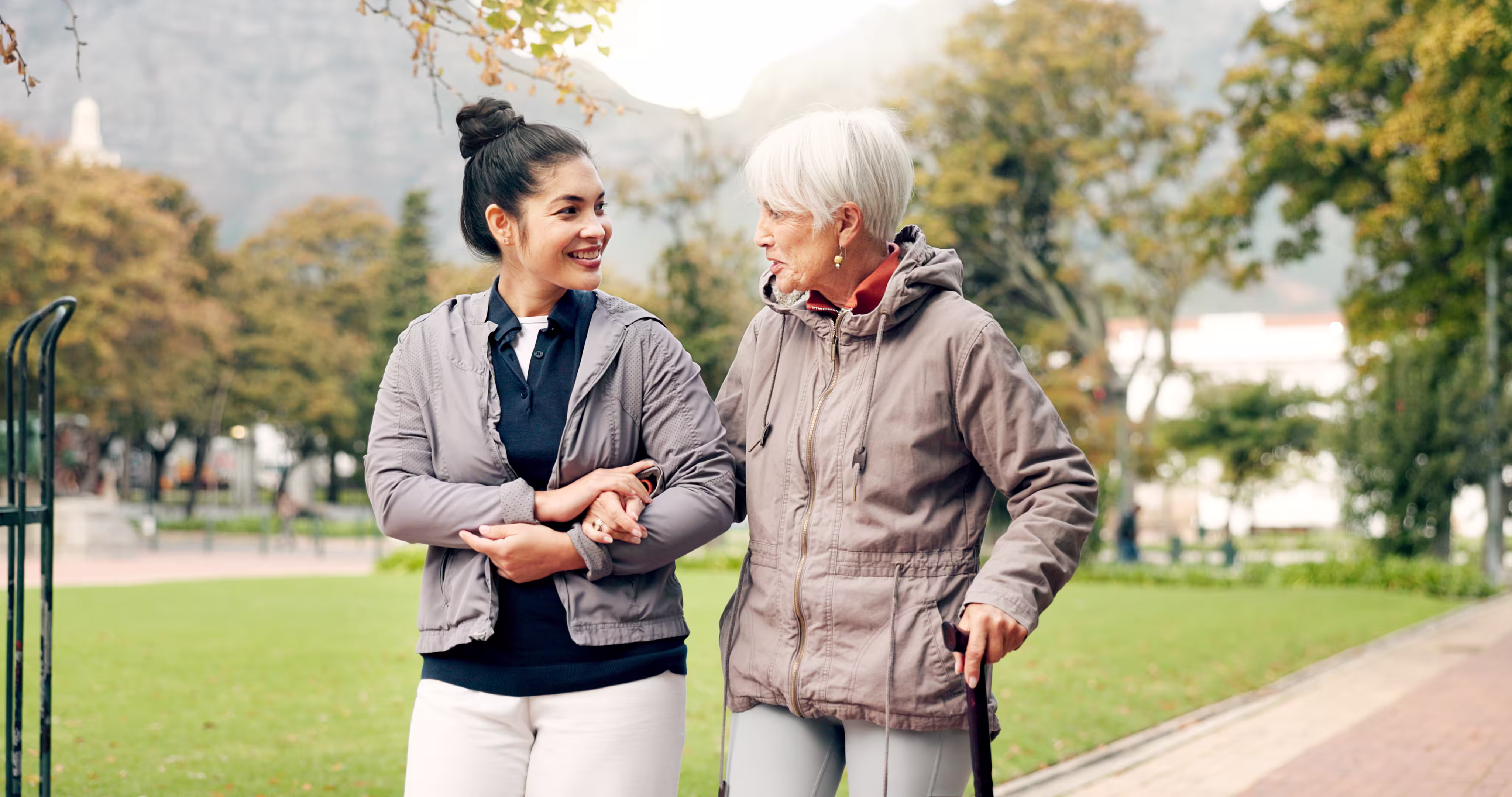female nurse in street clothes walks with elderly woman in park