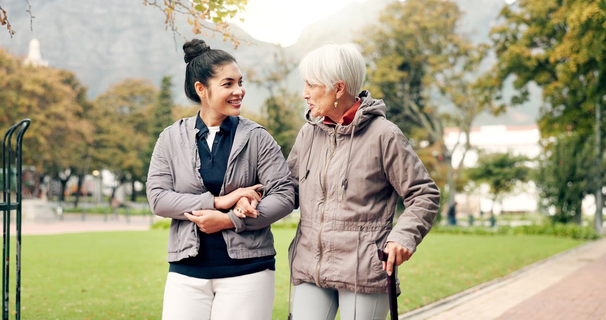 female nurse in street clothes walks with elderly woman in park