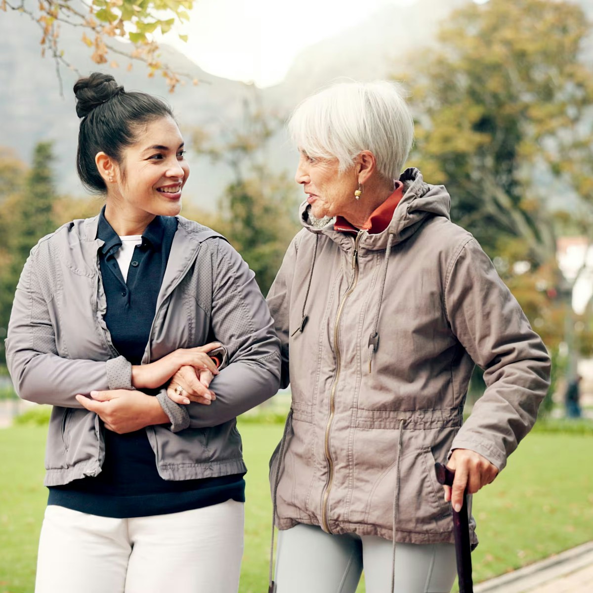 female nurse in street clothes walks with elderly woman in park