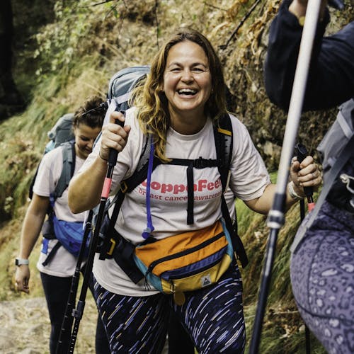 Gi smiling whilst on a trek, two walking sticks in hand.