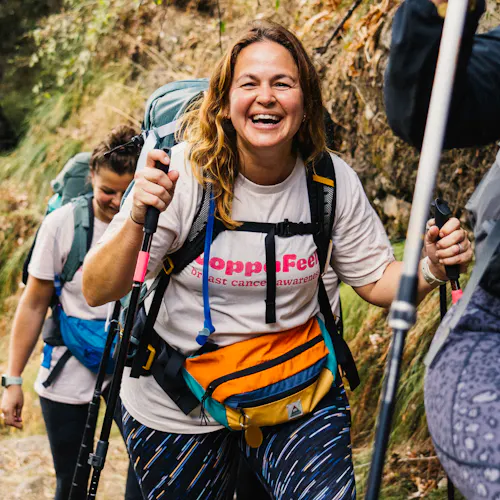 Gi smiling whilst on a trek, two walking sticks in hand.