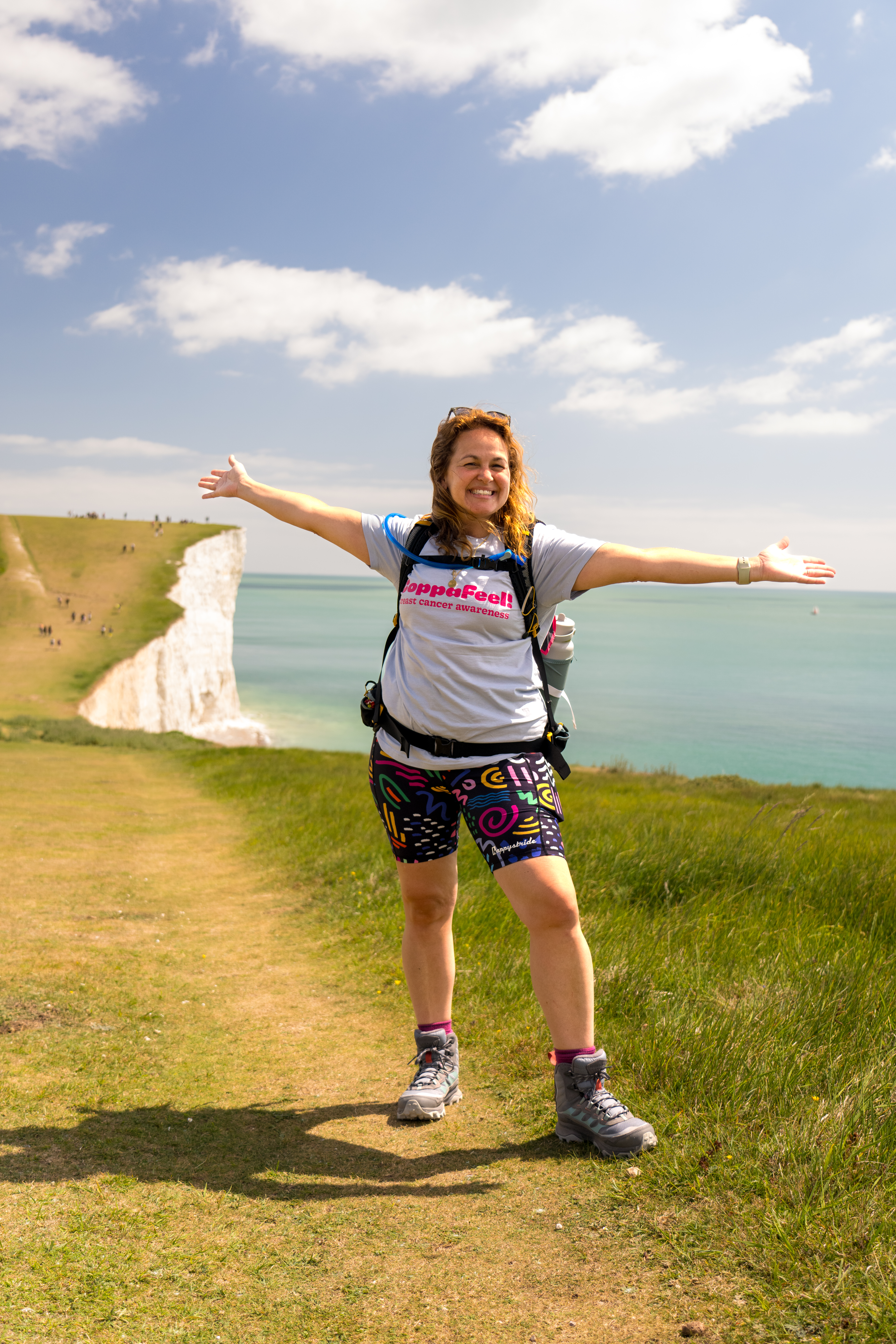 Gi smiling with arms outstretched in front of a grassy landscape