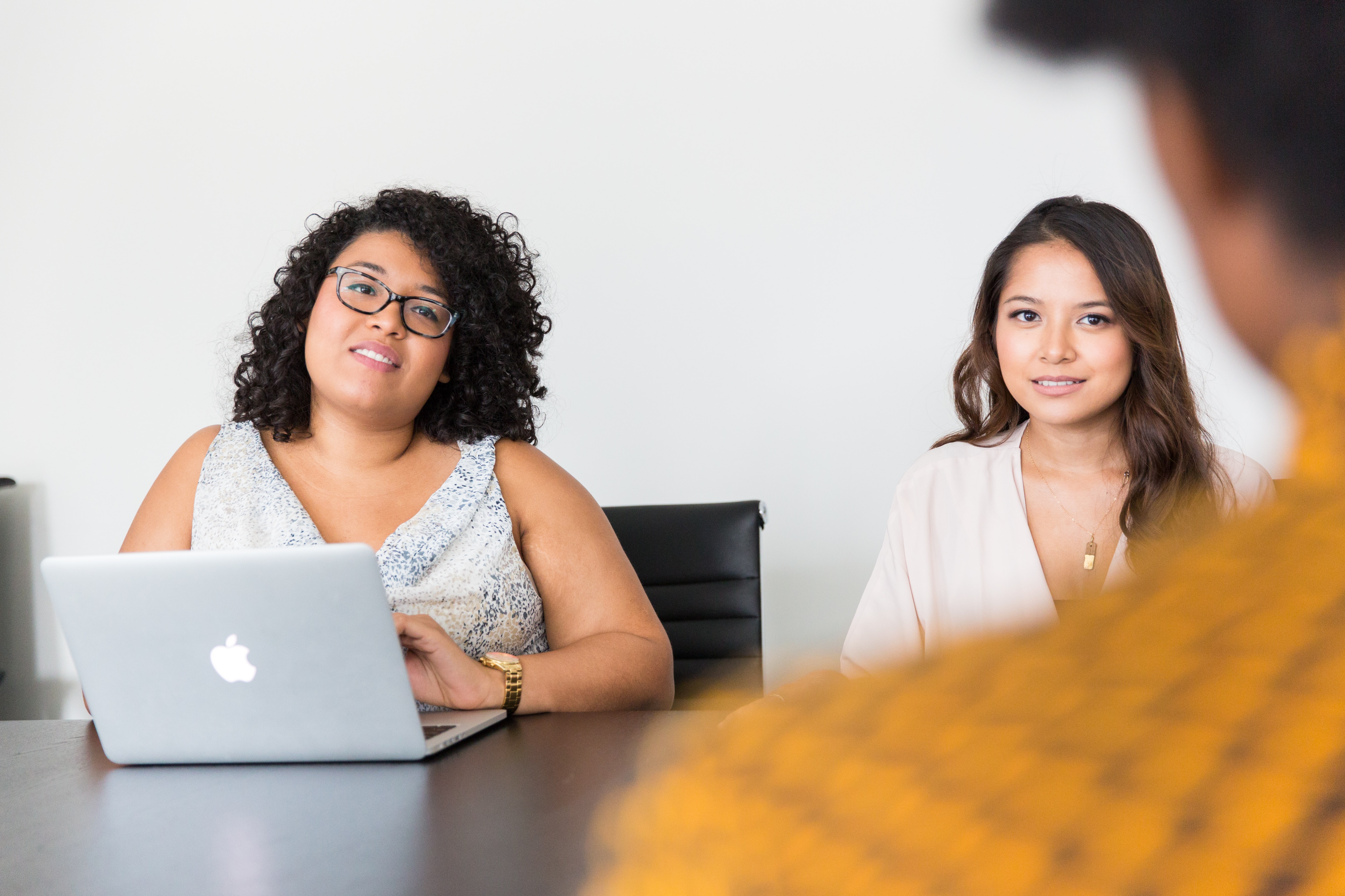 Two women sit across a table from an interviewee, over whose shoulder the photo is taken