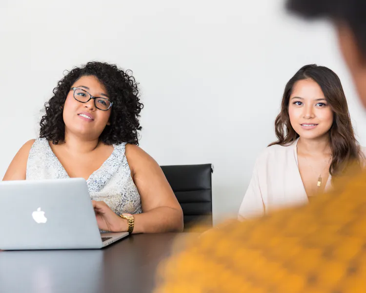 Two women sit across a table from an interviewee, over whose shoulder the photo is taken