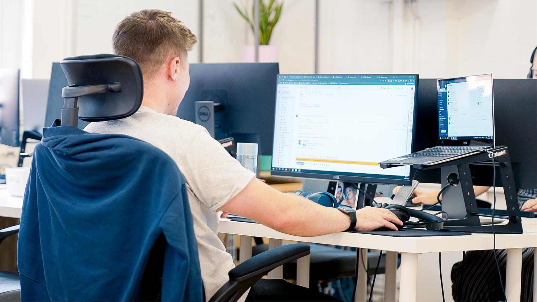 A man sits at a desk working on a laptop and a monitor