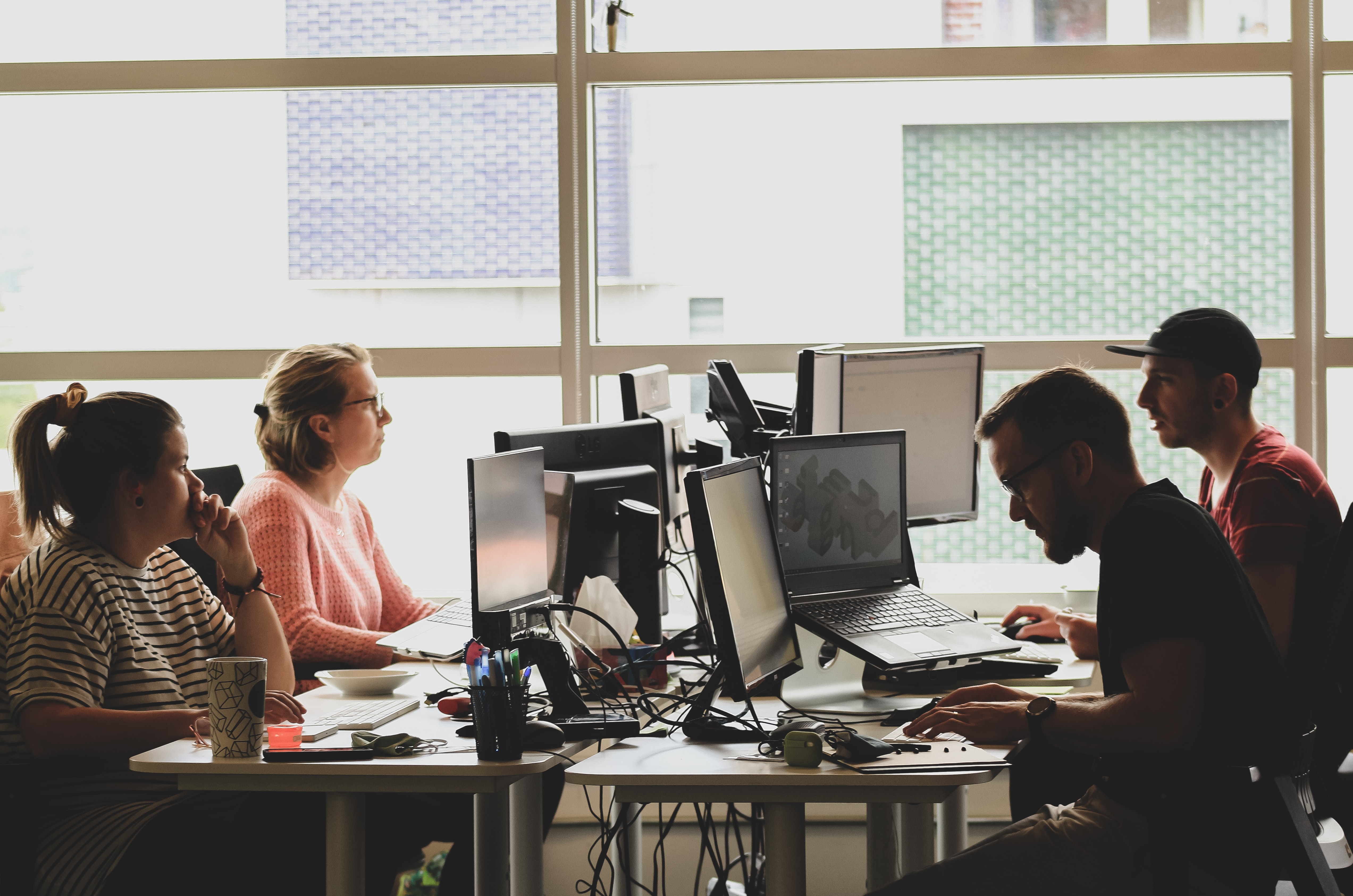 Four workers sitting at desks with computers and monitors