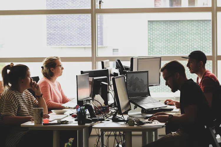 Four workers sitting at desks with computers and monitors