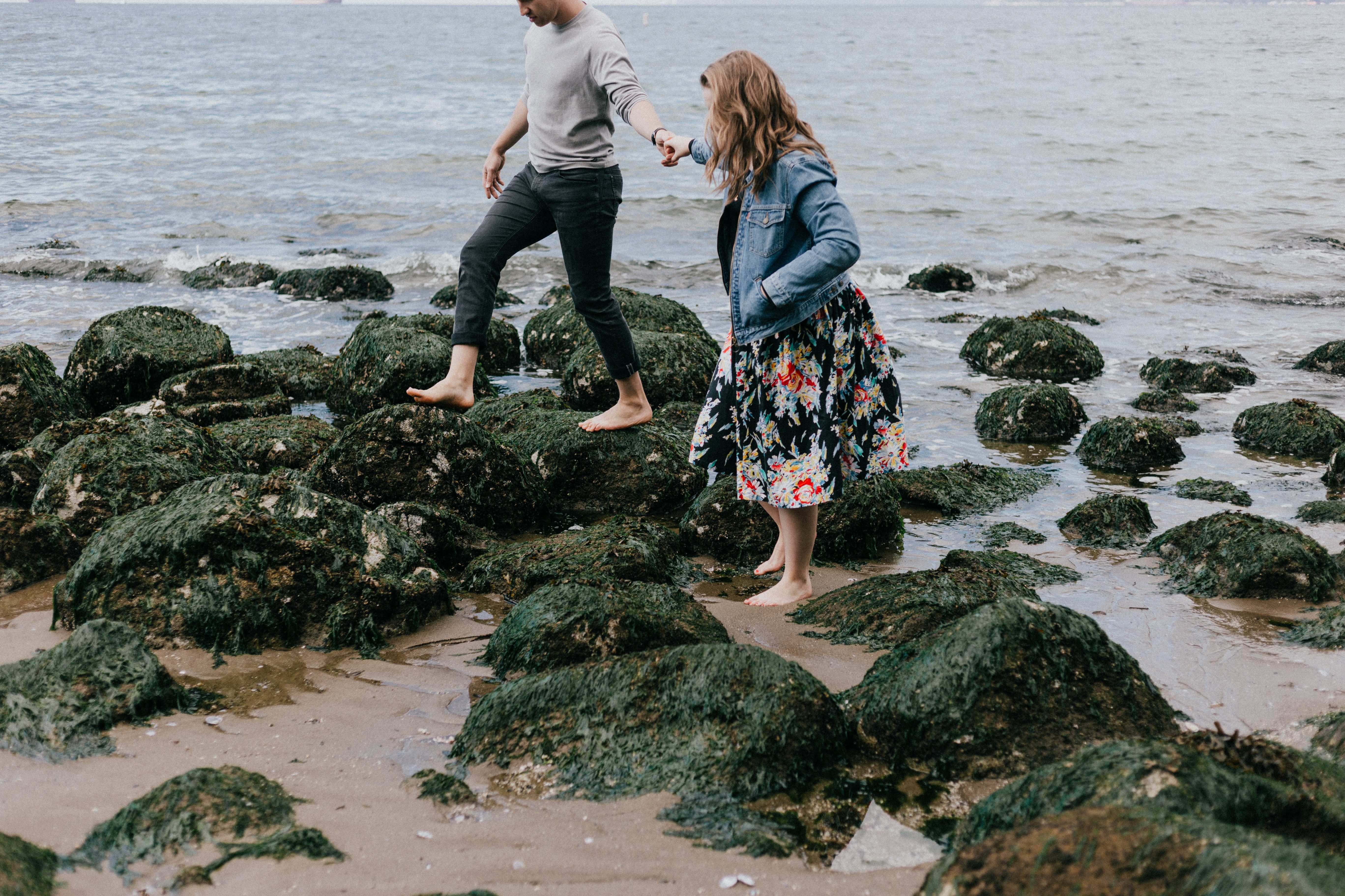 A man and a woman walking over rocks on a beach