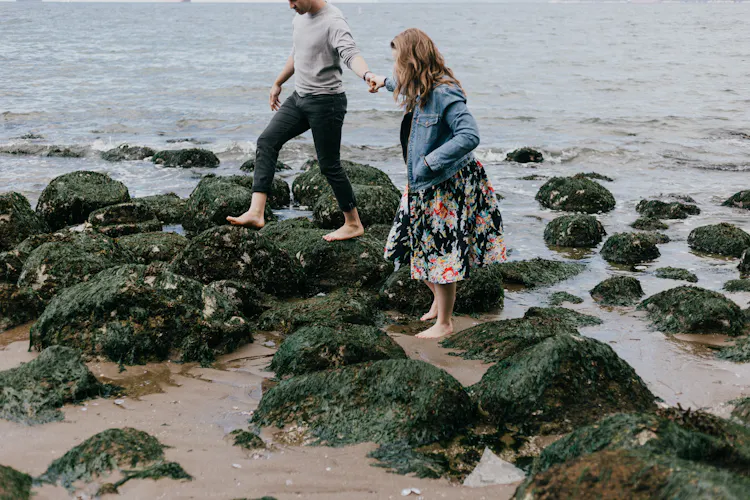 A man and a woman walking over rocks on a beach