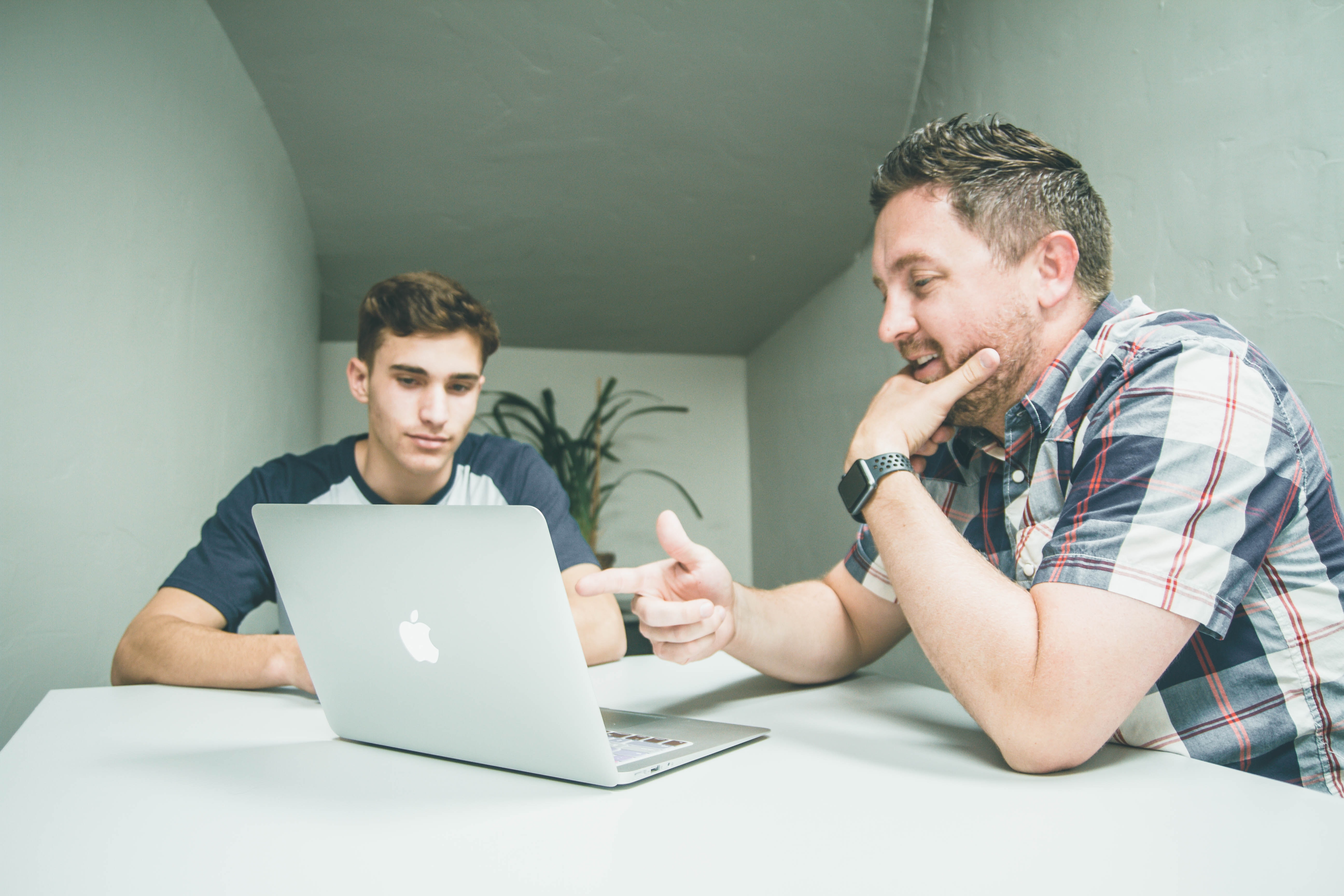 Cover of A young man and a slightly older man sit at a desk looking at a macbook article