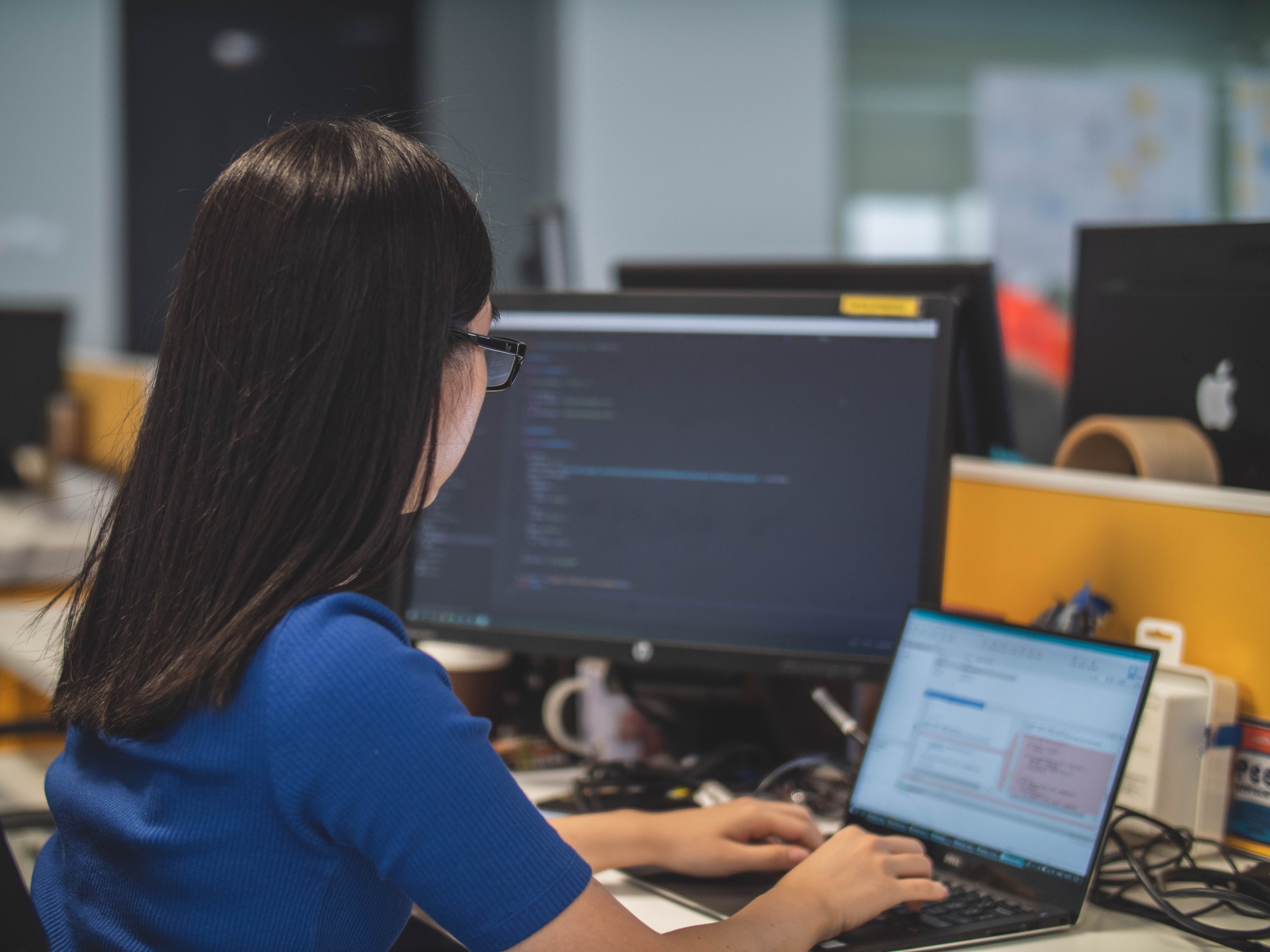 Cover of Woman sitting at a desk working on a laptop with code on a monitor article