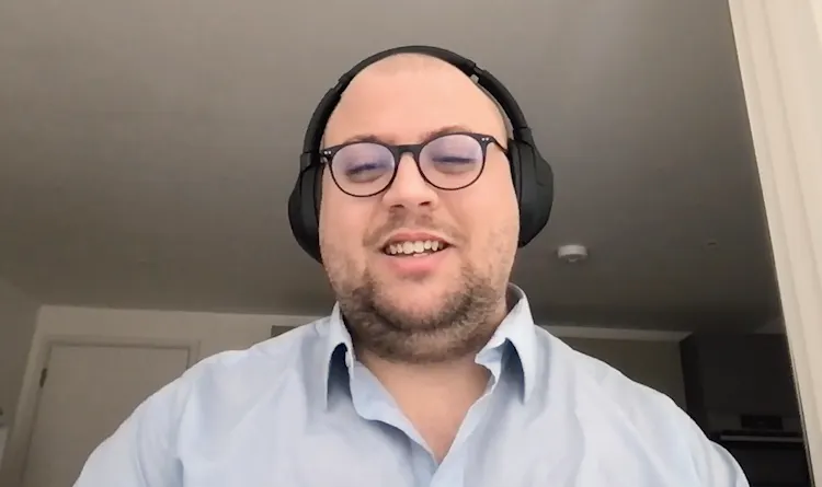 Smiling man with glasses sits in front of computer