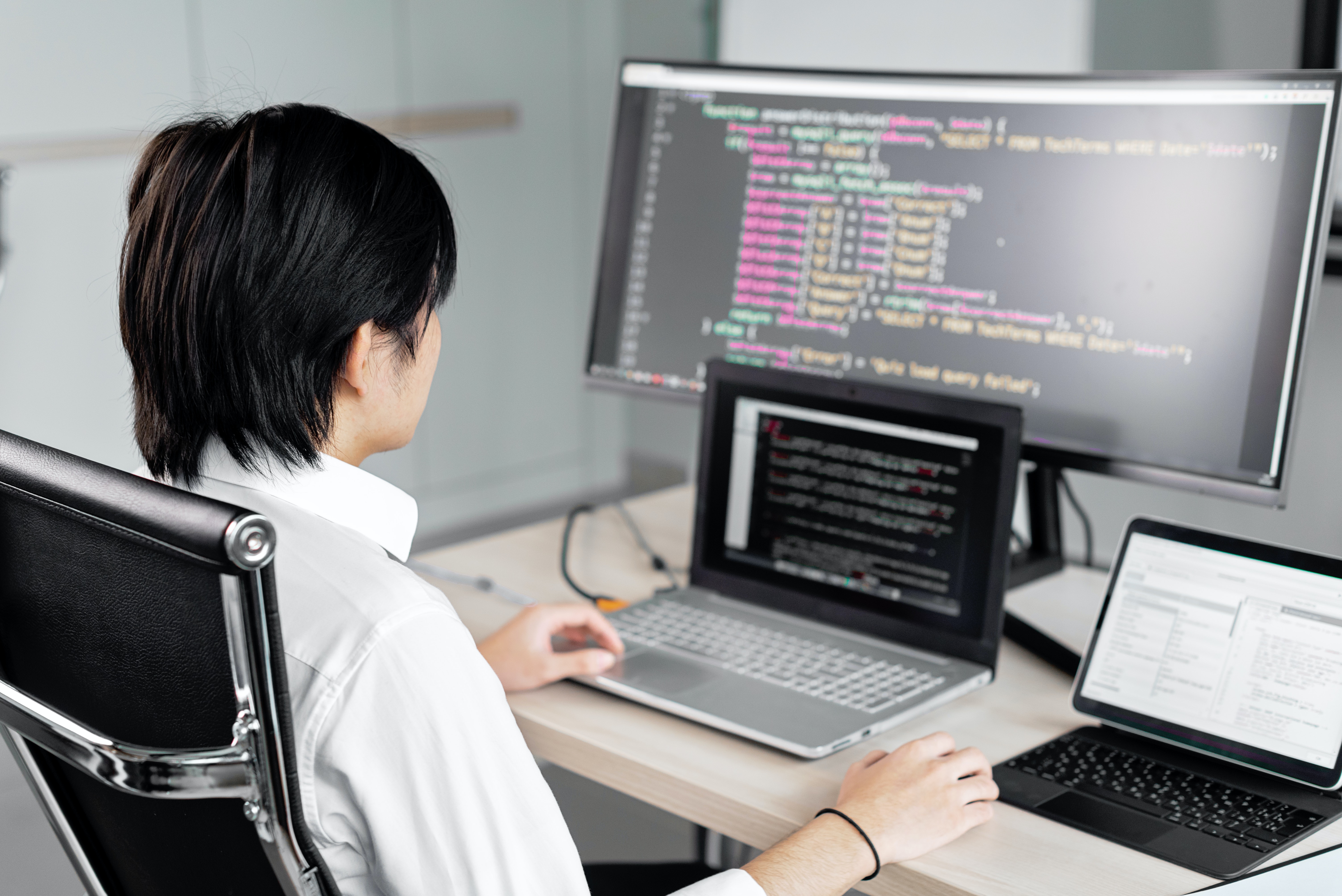 Cover of Man sitting at a desk looking at code on a monitor with two laptops article