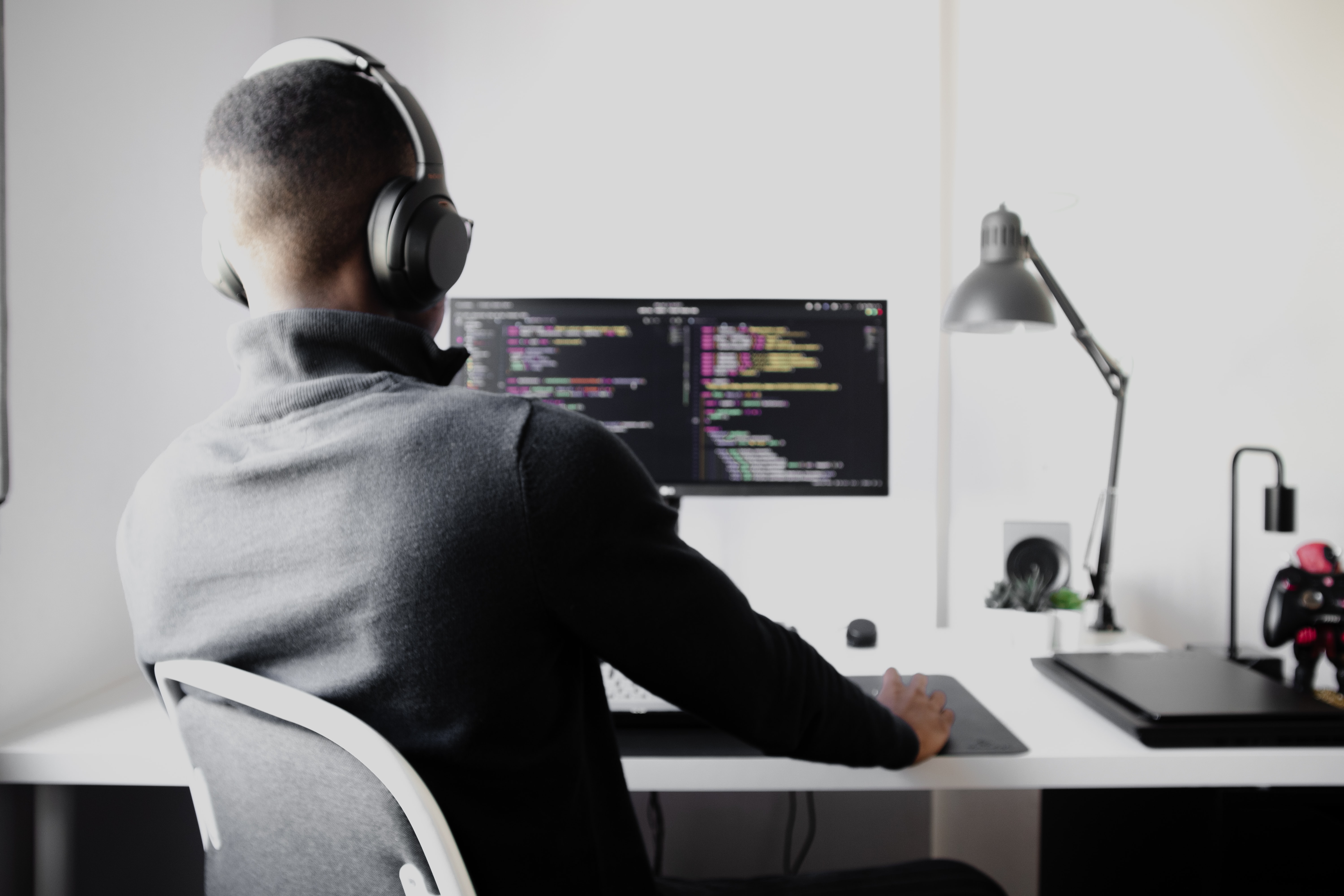 Cover of Man sitting at a desk with code on monitor, wearing headphones article