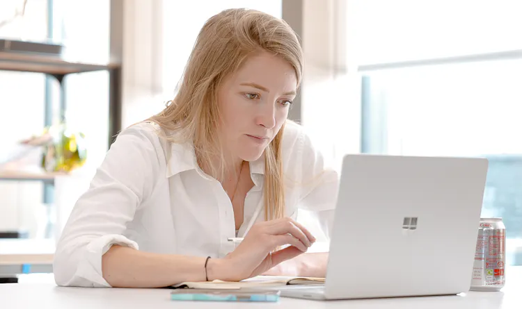 Cover of A woman sitting at a desk in a brightly lit office looking at a laptop article