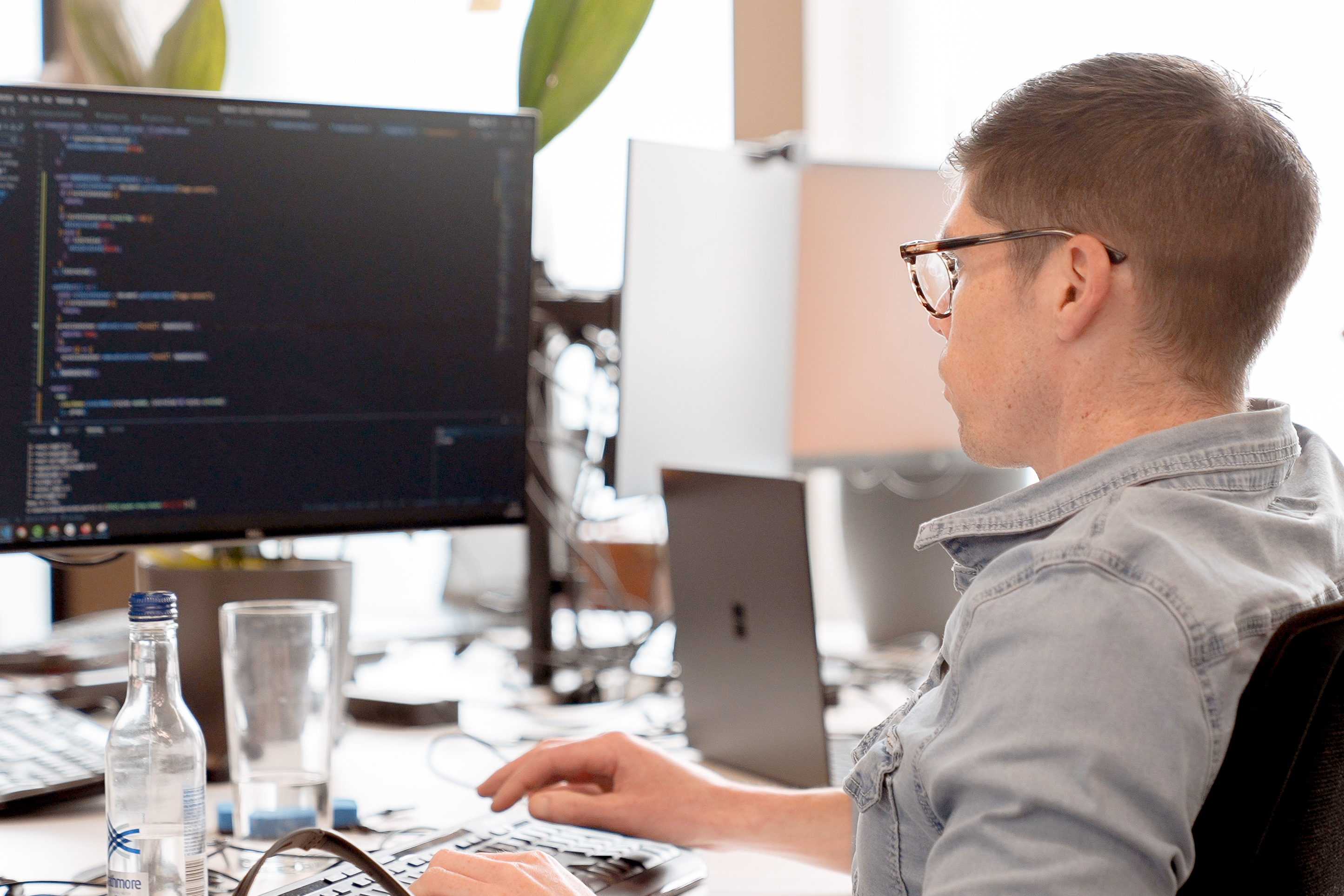 Cover of A man sitting in a brightly lit office looking at code on a monitor article