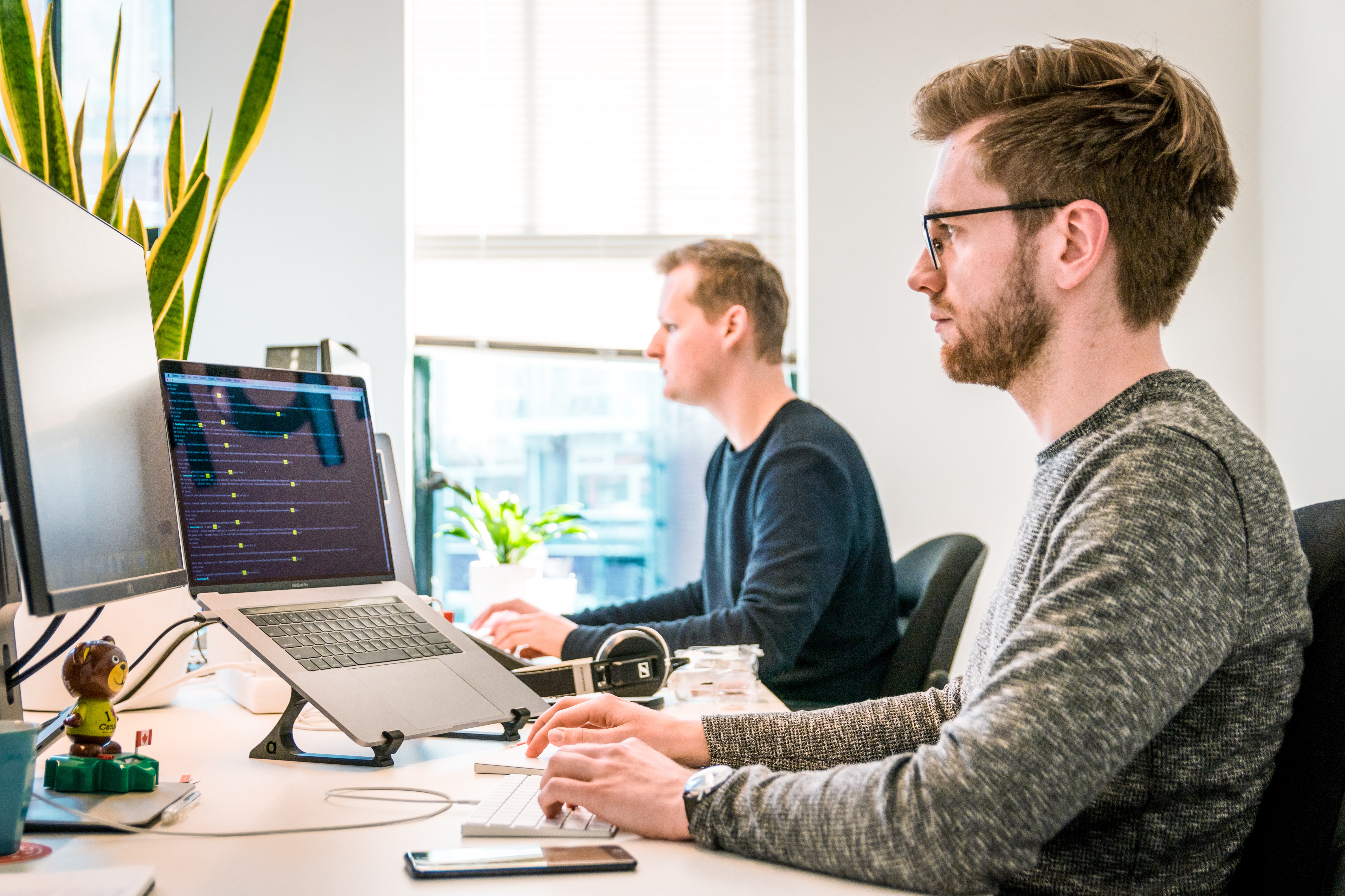 Cover of Two men sitting at a desk working on laptops article