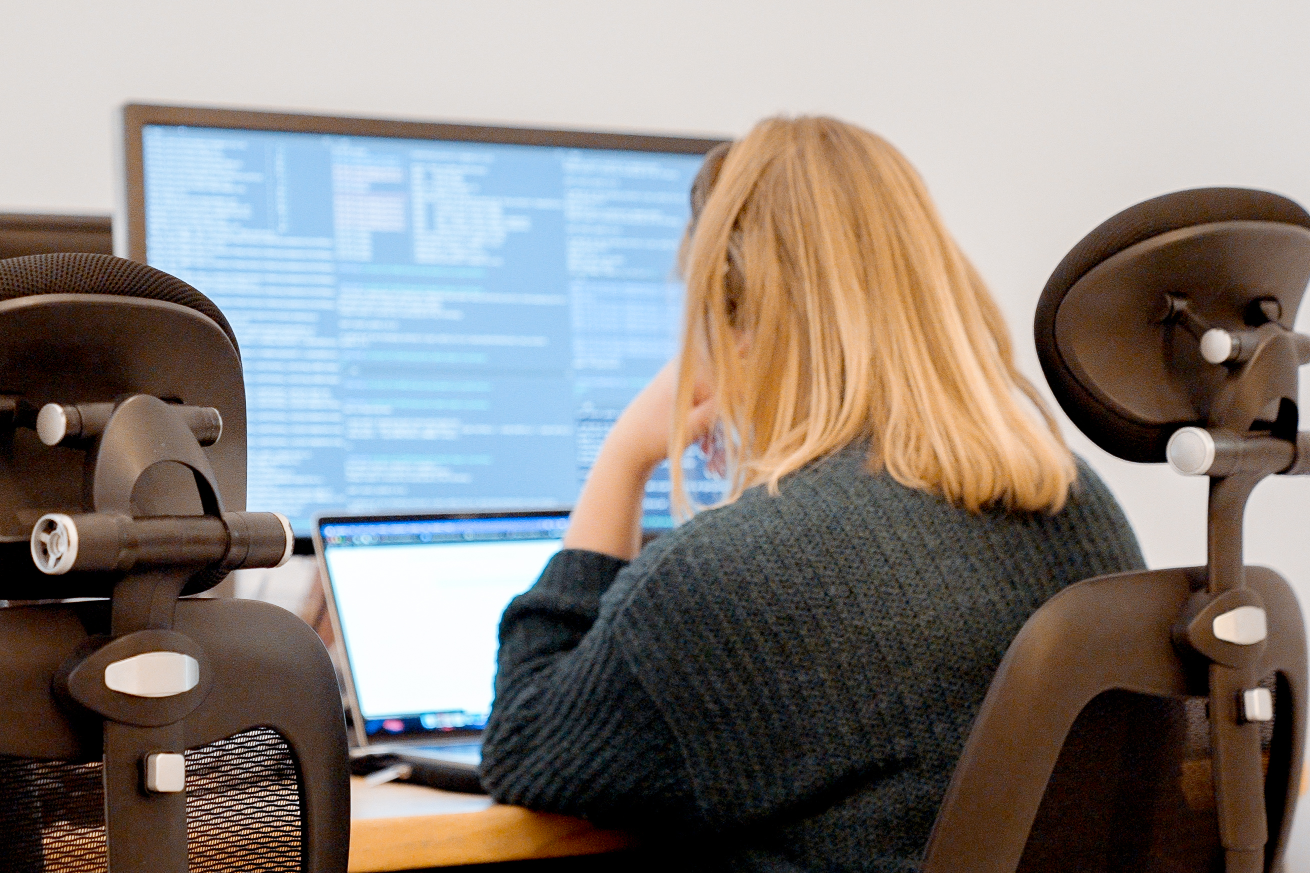 Cover of A woman is seen from behind sitting at a desk looking at code on a screen article