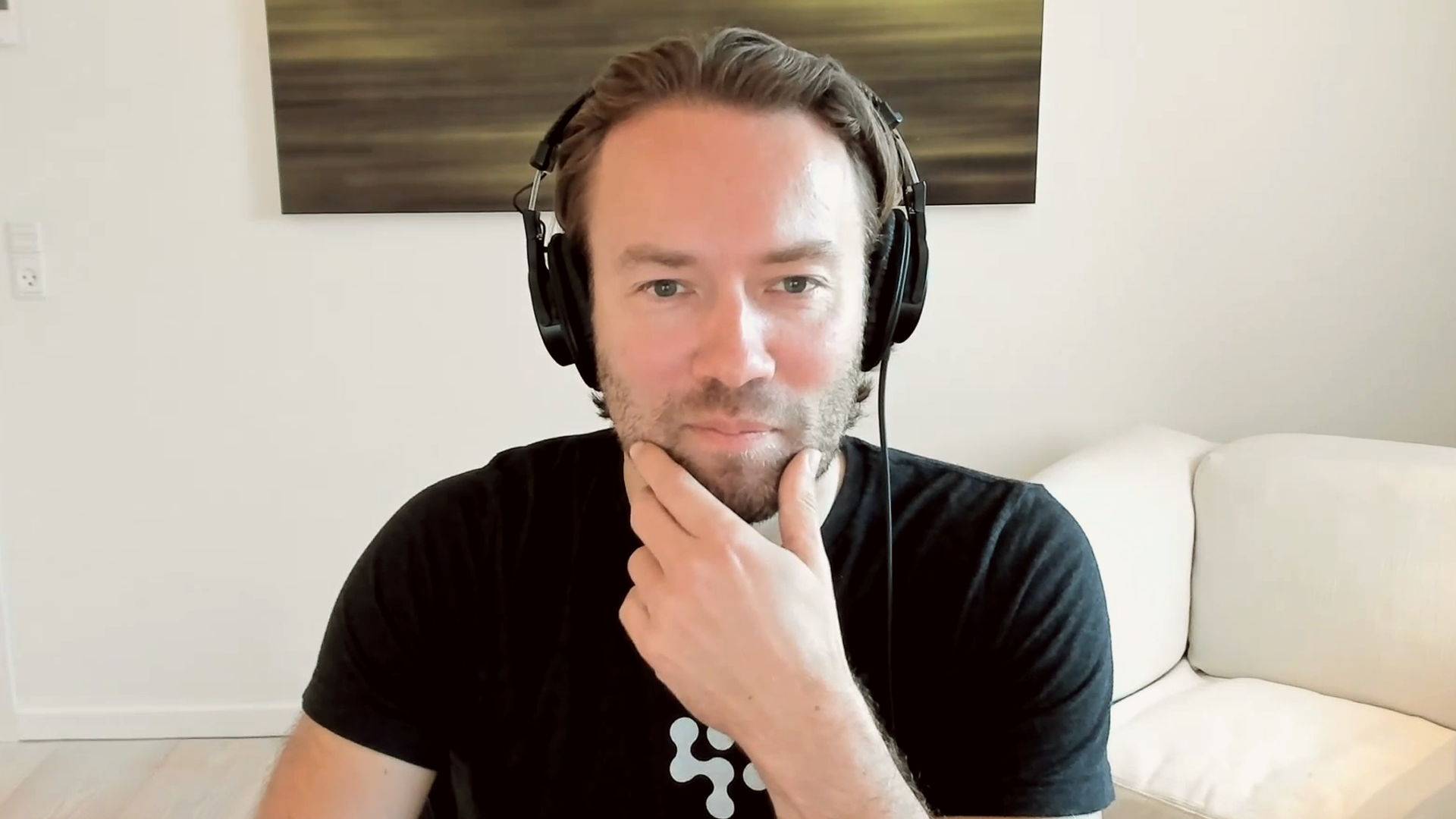Man wearing headphones touches chin sitting in front of computer
