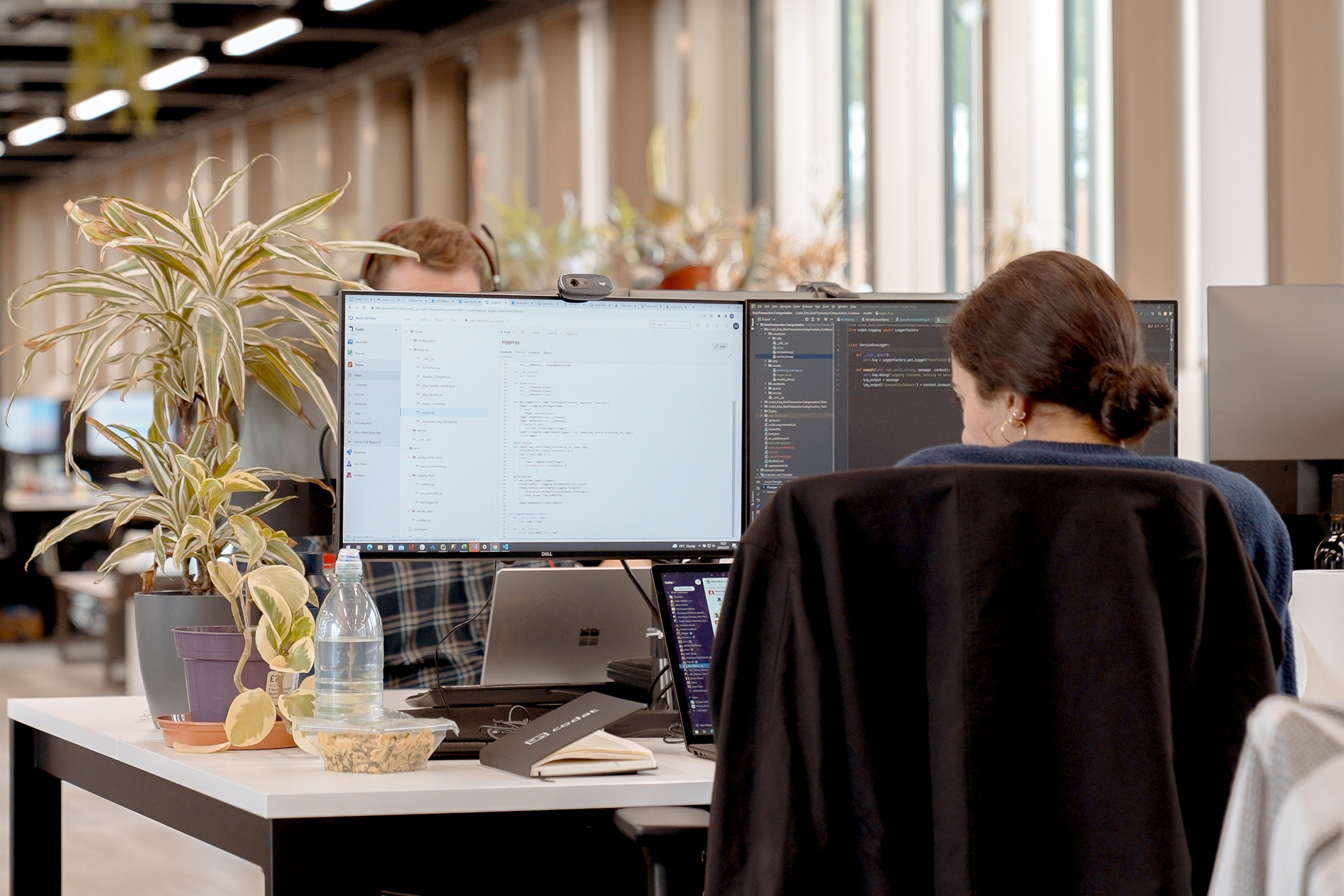 A woman sits in an office with her back to the camera looking at code on a monitor