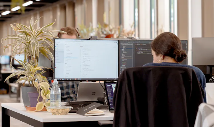 A woman sits in an office with her back to the camera looking at code on a monitor
