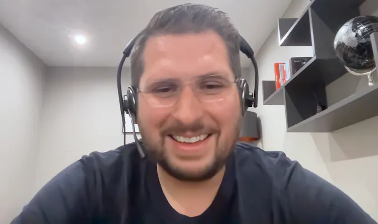 Man with glasses and headphones smiles in front of computer