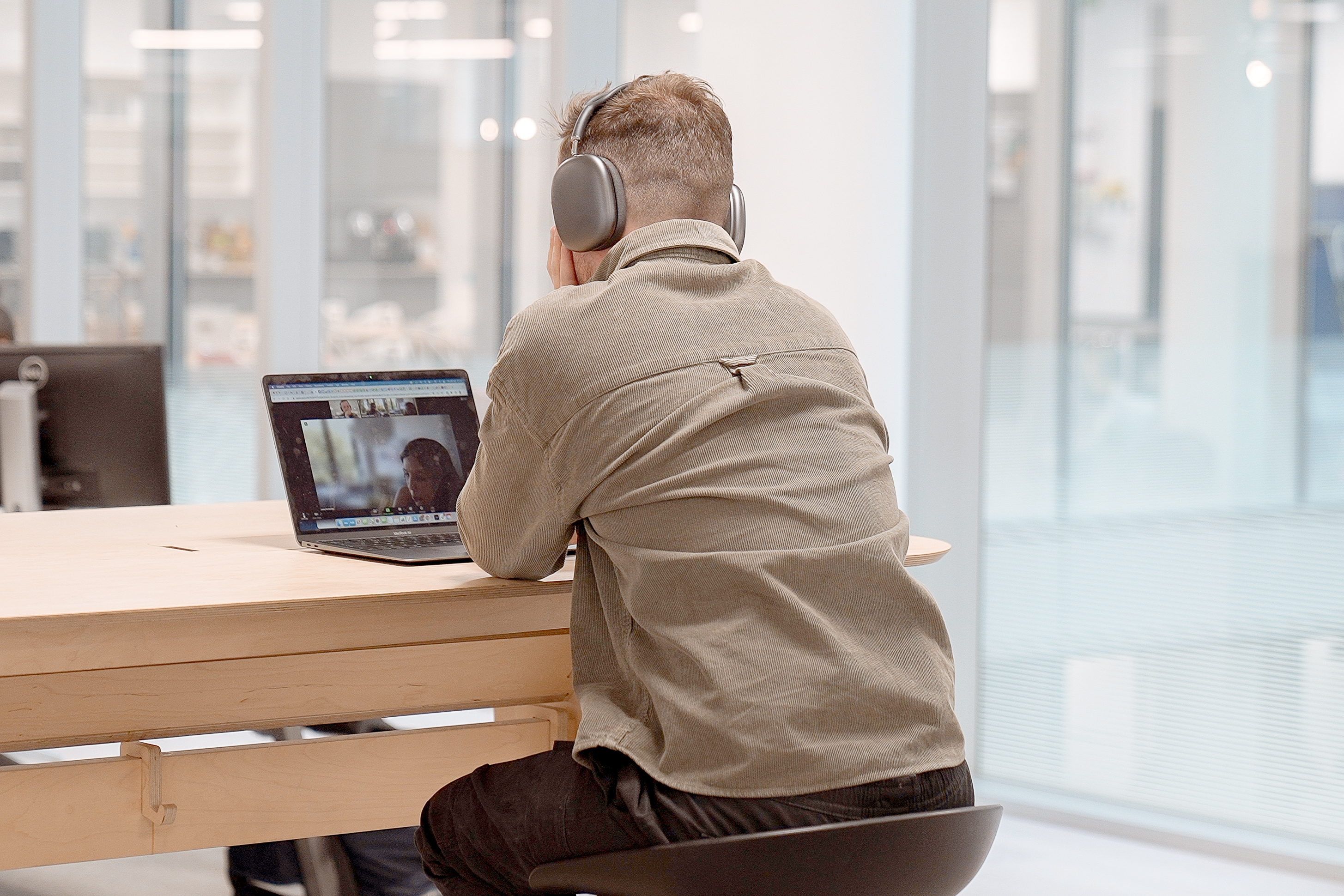 A man wearing headphones with his back to the camera, in an office speaking on a conference call