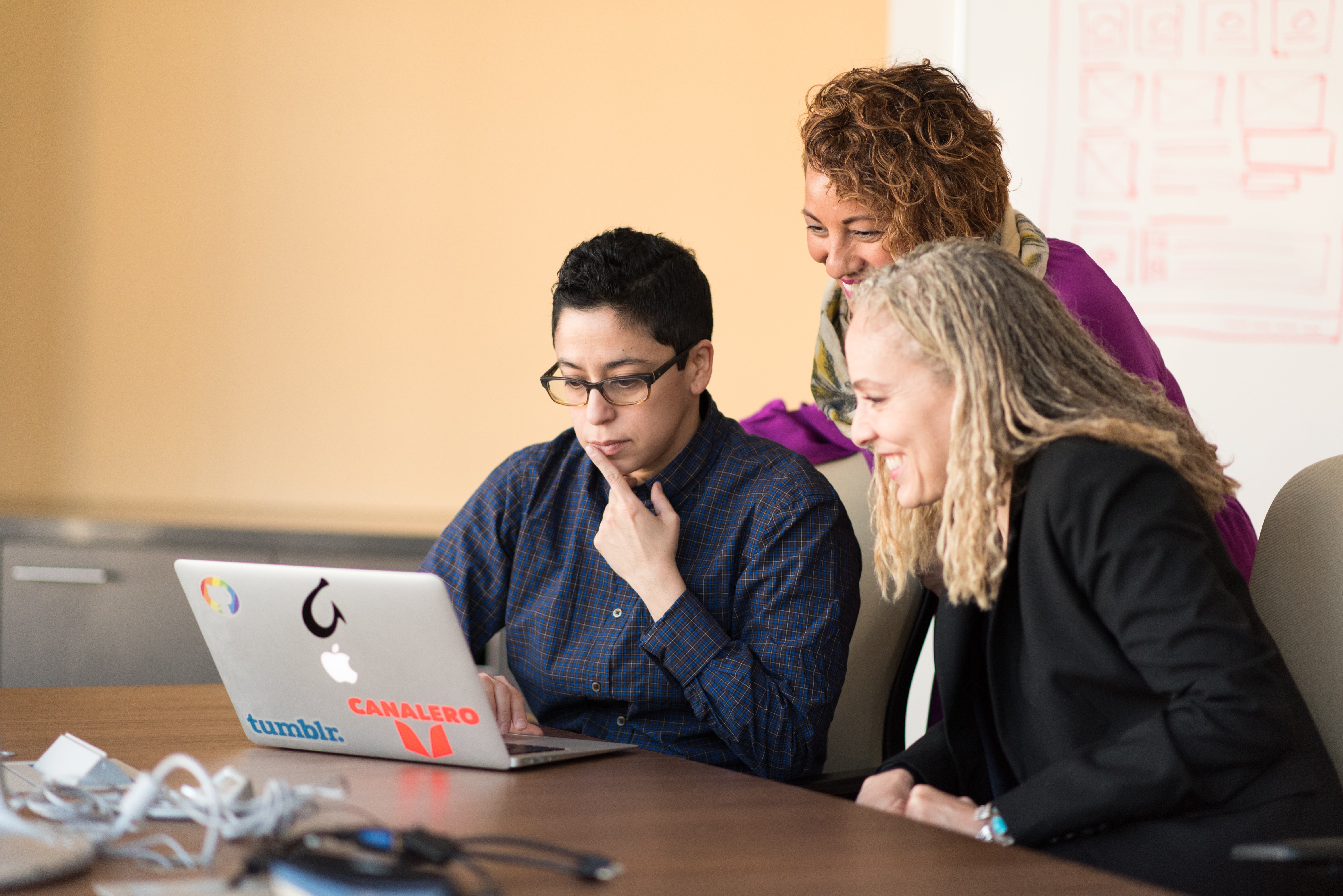 Three women sitting at a desk looking at a laptop