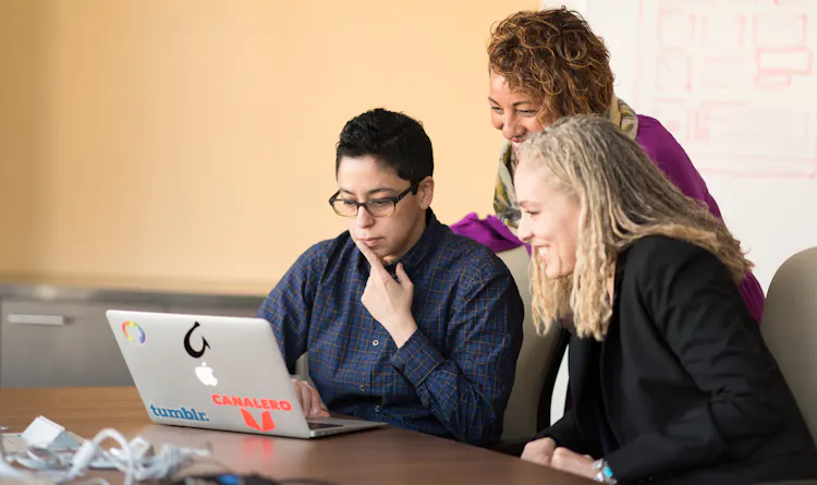 Three women sitting at a desk looking at a laptop