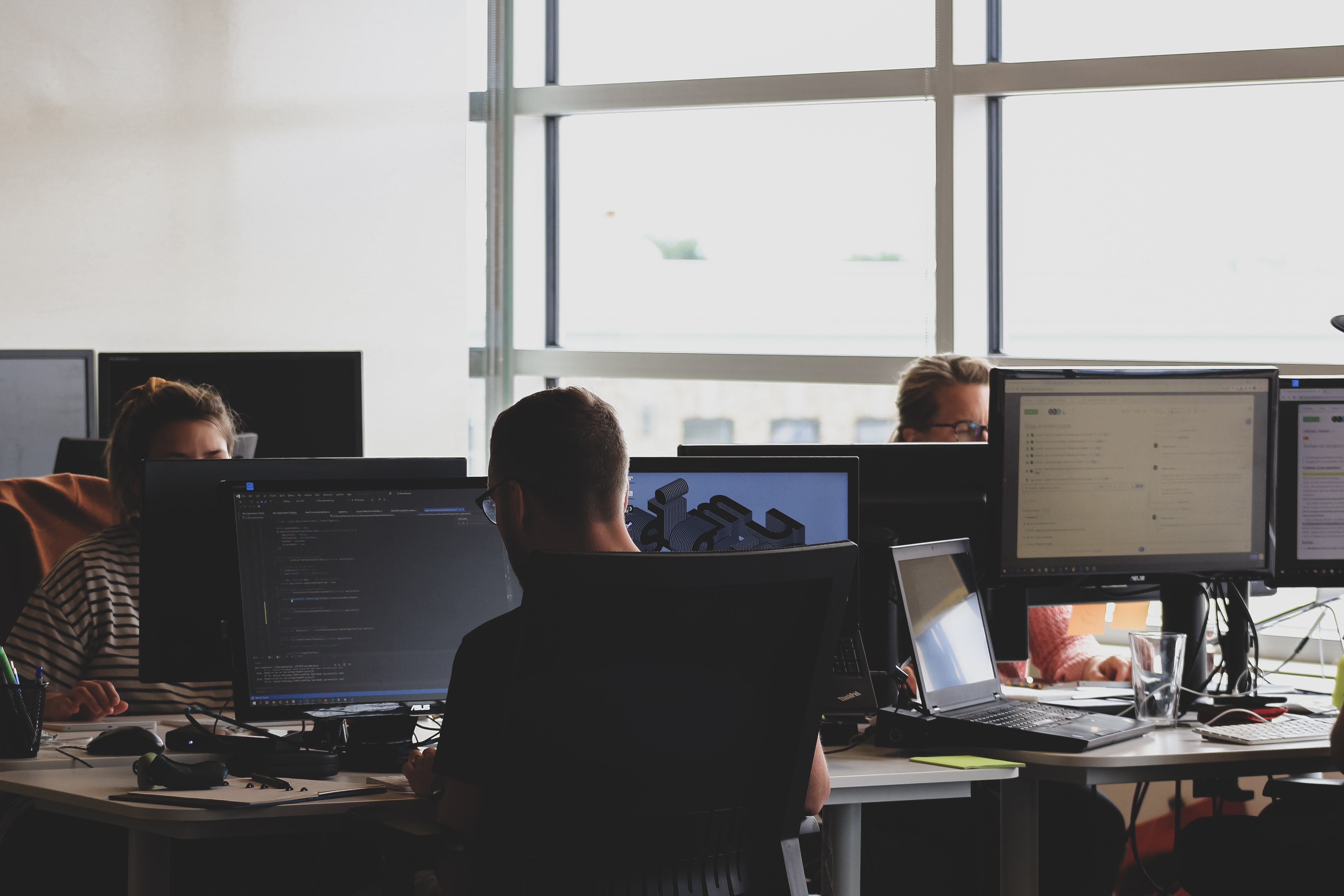 Cover of Three developers sitting at a bank of desks working on code article