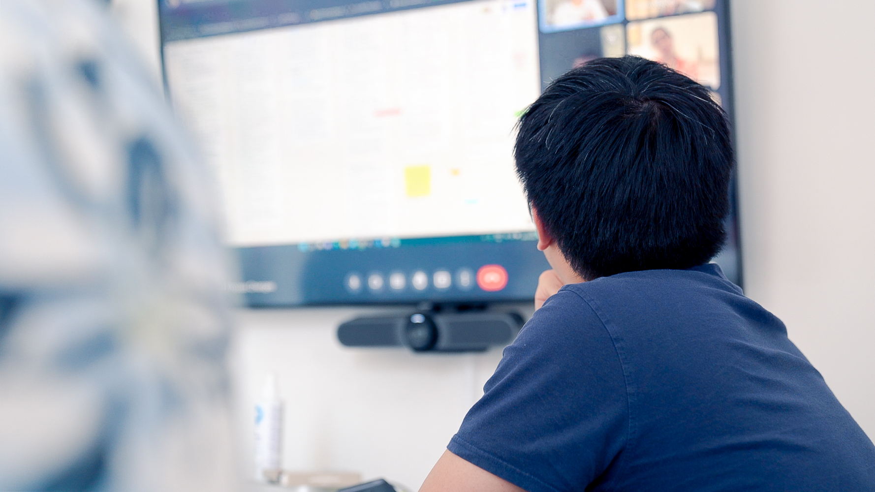 A man seen from behind looks towards a large conference call screen
